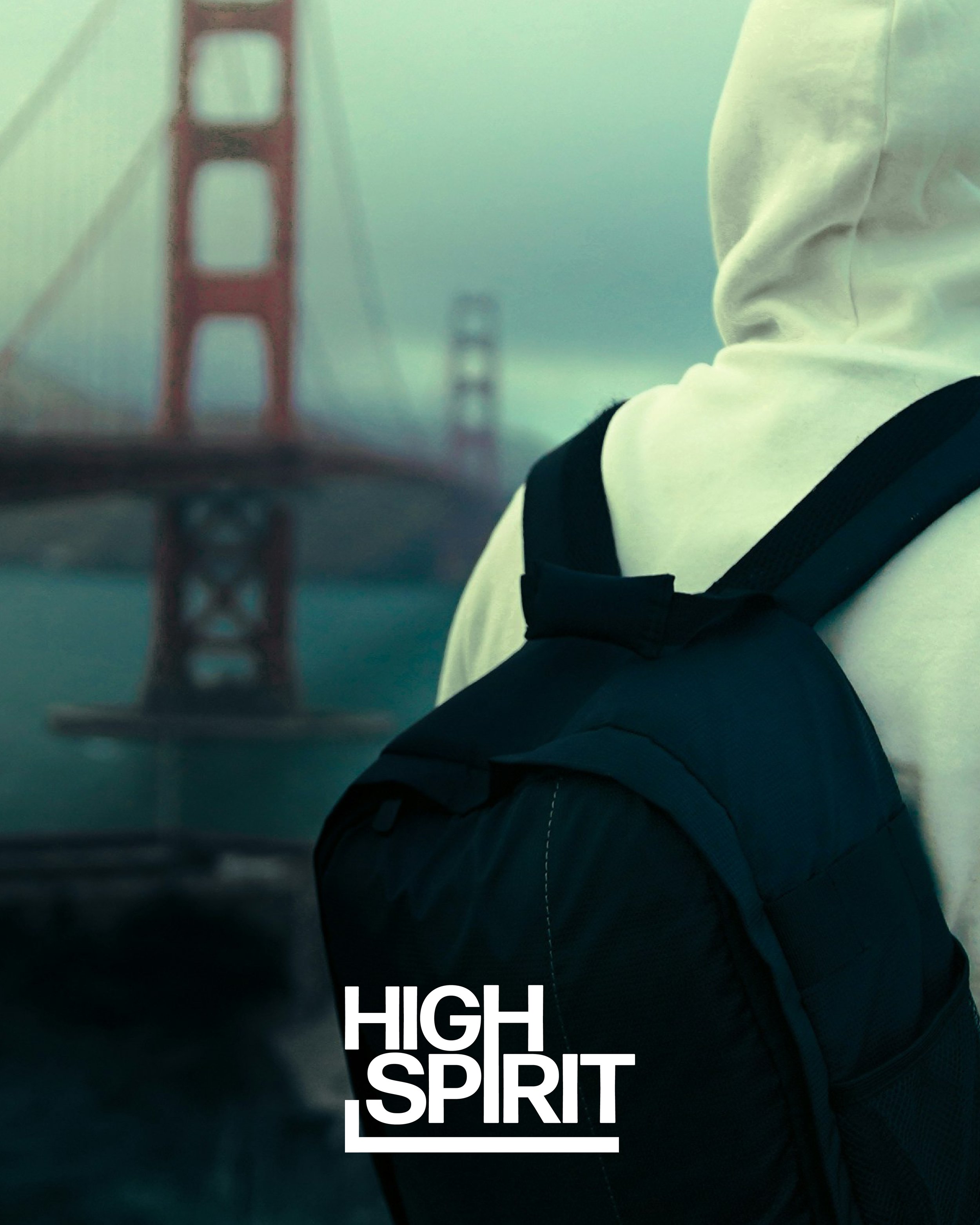 Close-up of a person wearing a black jacket with white text that reads 'HIGH SPIRIT' against a background featuring a bridge with red towers and greenish fog.