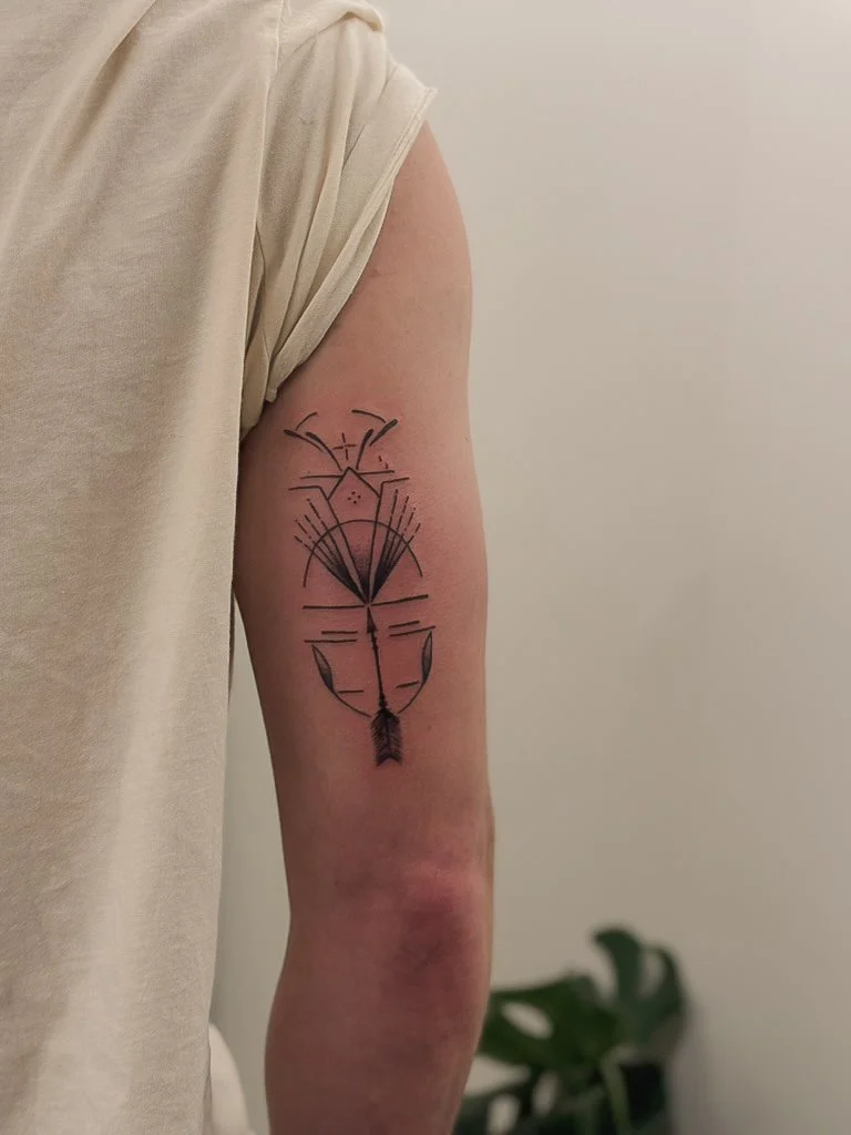 Tattoo of a geometric abstract design on a person's upper arm, with lines, shapes, and a black arrow at the bottom.
