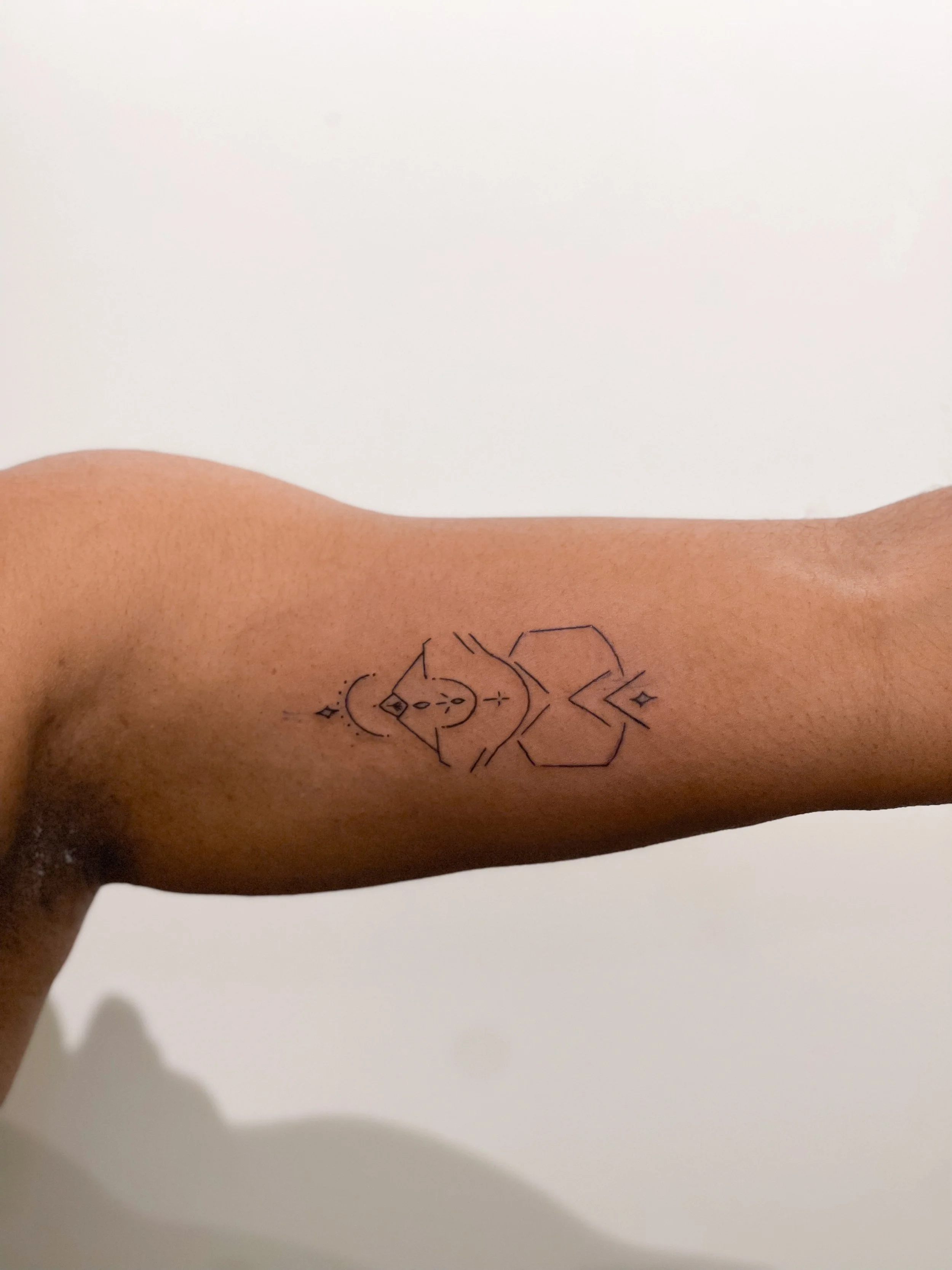 A person's upper arm with a geometric tattoo design on the inside of the bicep.