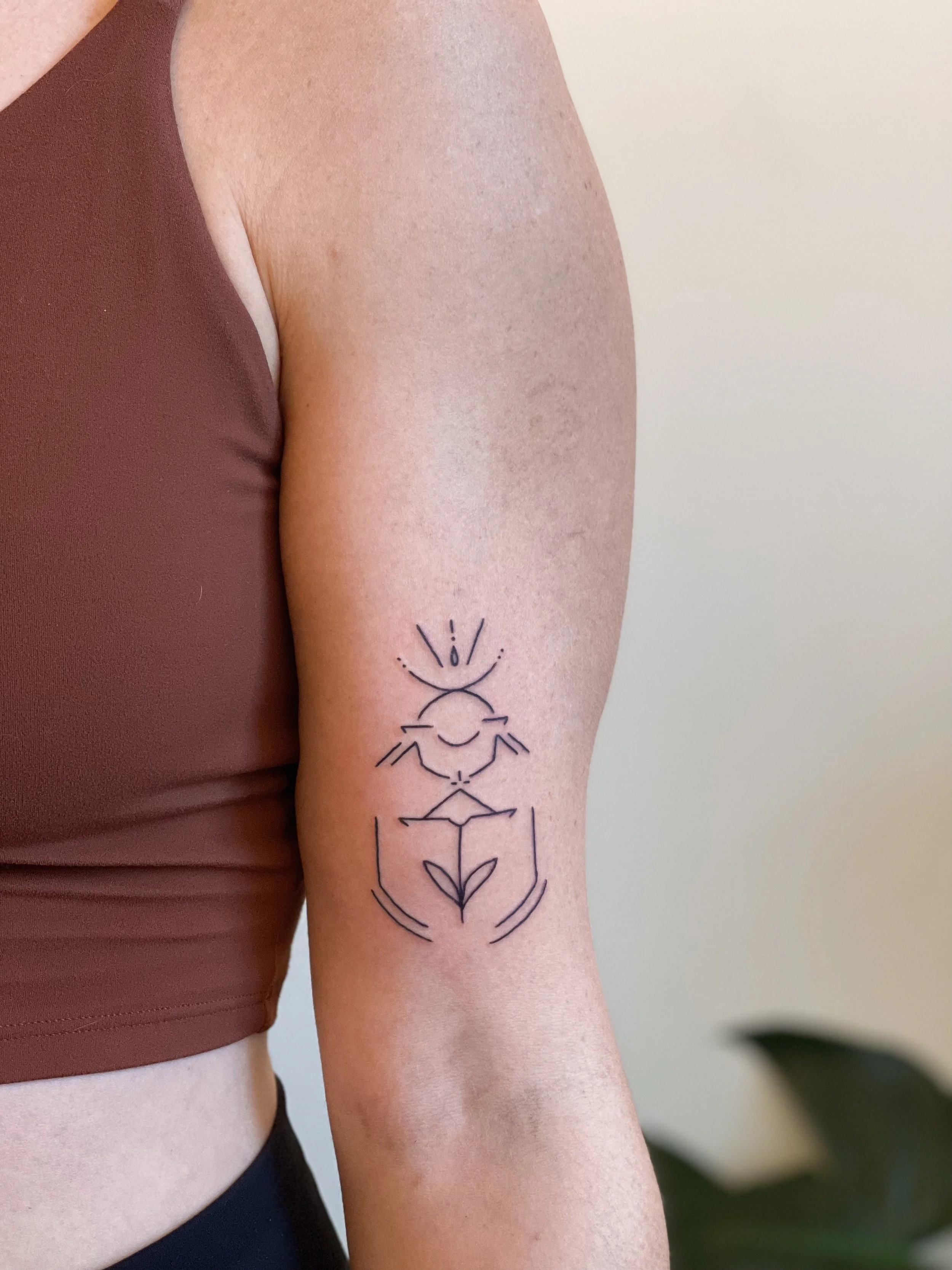 A tattoo of a minimalist line drawing of a bee, flower, and hands on a person's upper arm.