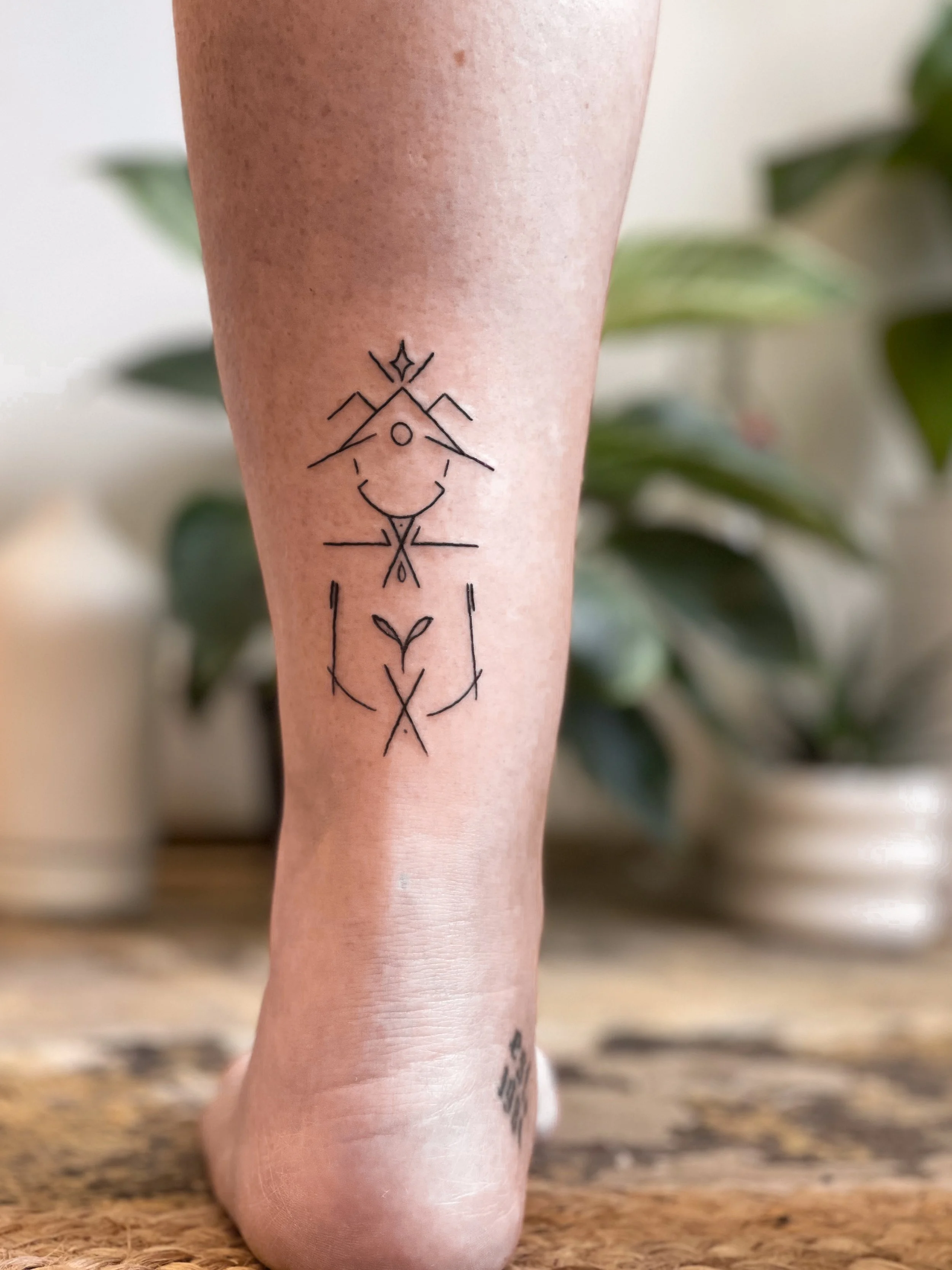 Tattoo of a minimalist geometric line drawing on a person's calf, featuring abstract shapes resembling a face and a figure with a crown on the head.