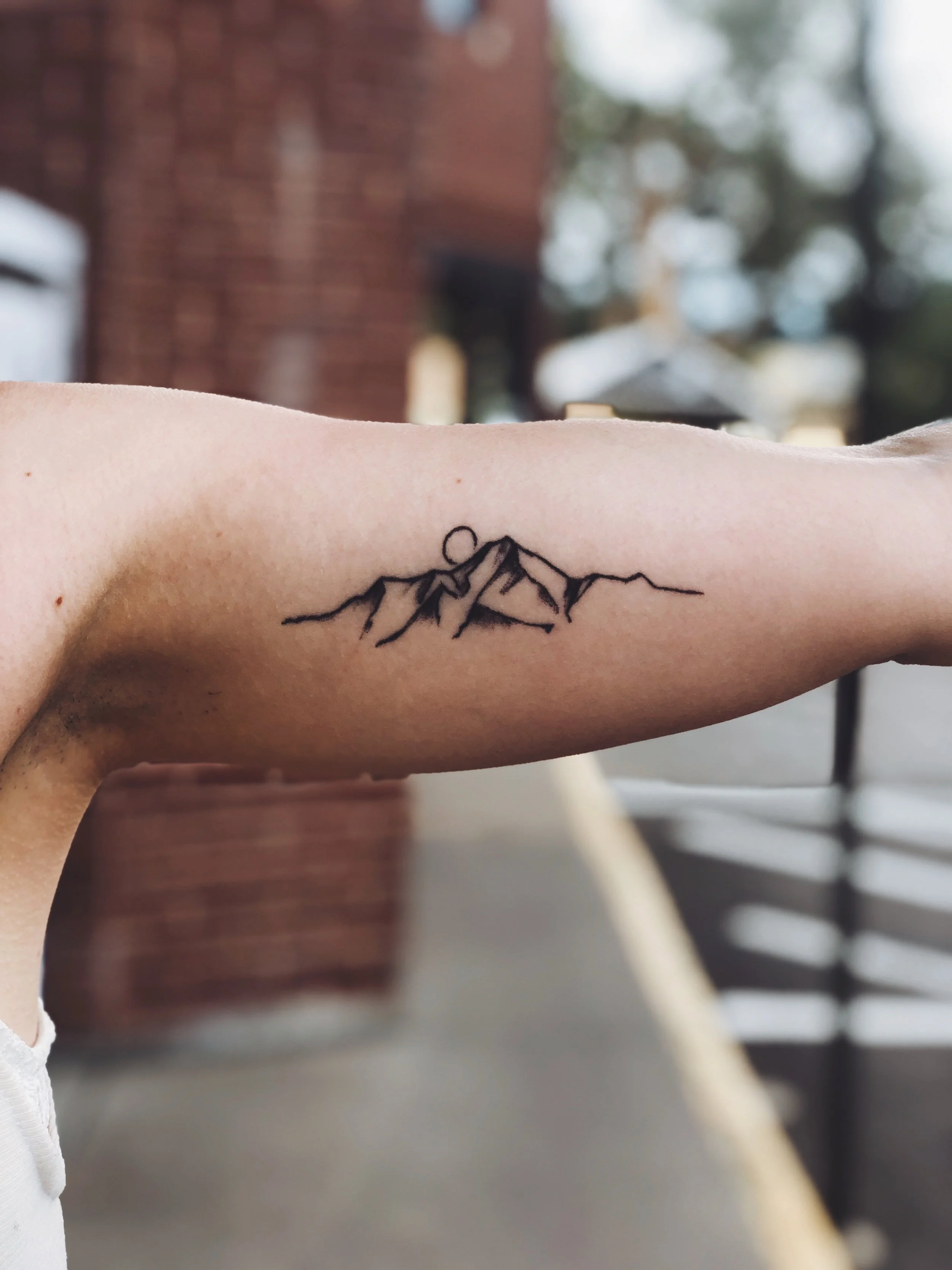 A tattoo of a mountain range with a sun or moon rising or setting behind the peaks, on a person's arm.