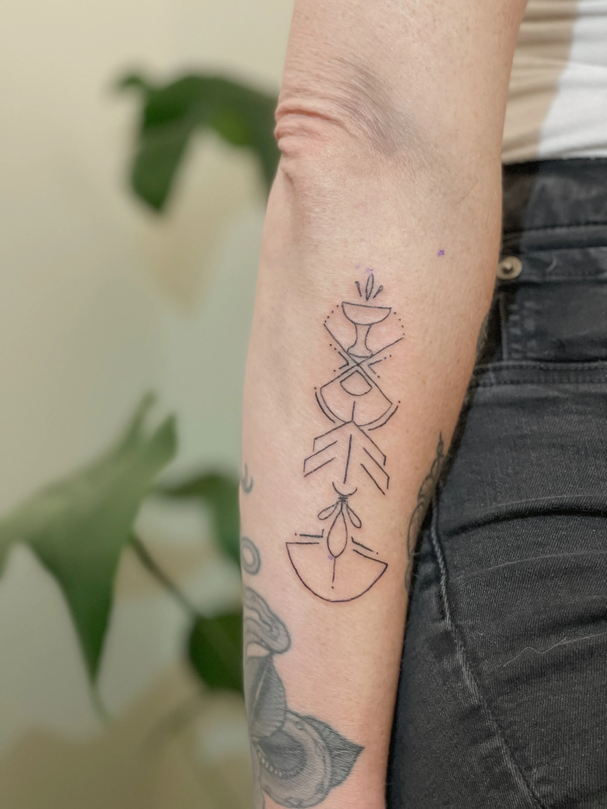 Line art tattoo on person's forearm featuring geometric and abstract shapes, a wine glass, and a cup with steam.