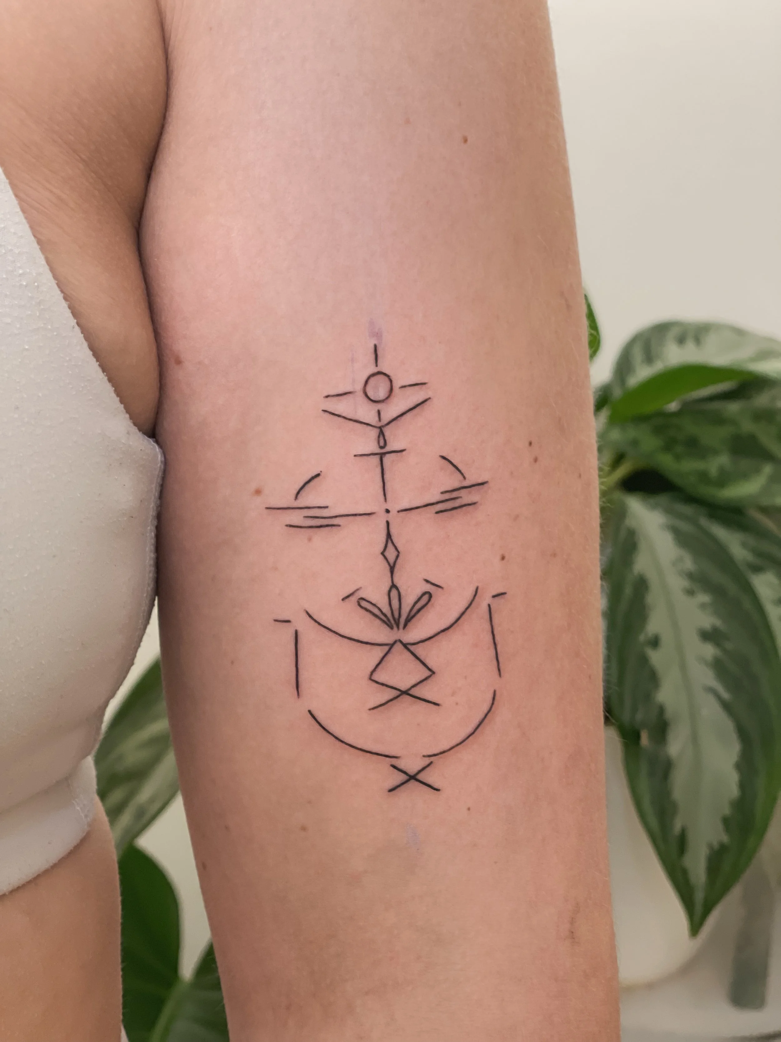 Black geometric tattoo on person's upper arm with symmetrical lines, circles, and triangles, and a crescent shape.