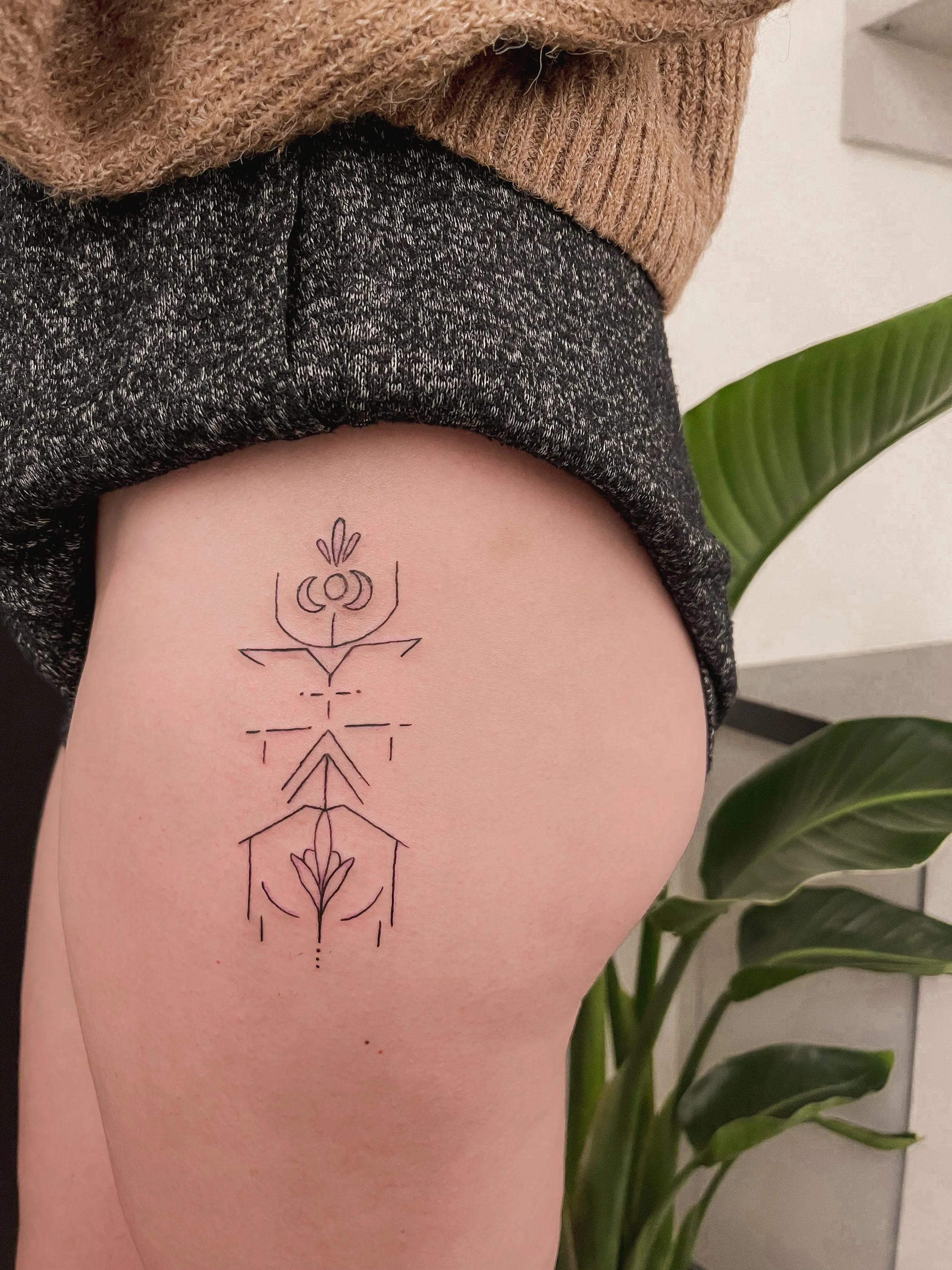 A tattoo of a geometric and line art design on a person's upper thigh, featuring symmetrical floral and abstract elements.