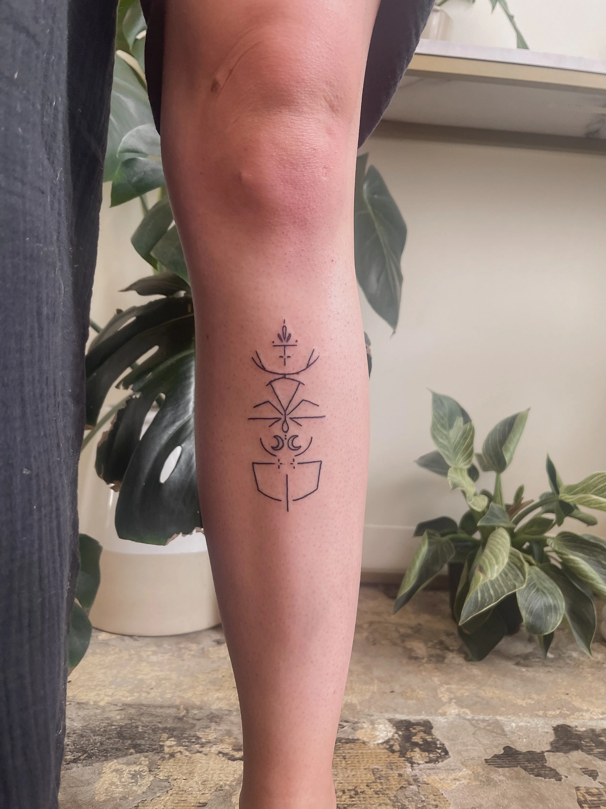 A person's leg with a black geometric tattoo on the calf, featuring symmetrical lines, shapes, and symbols.