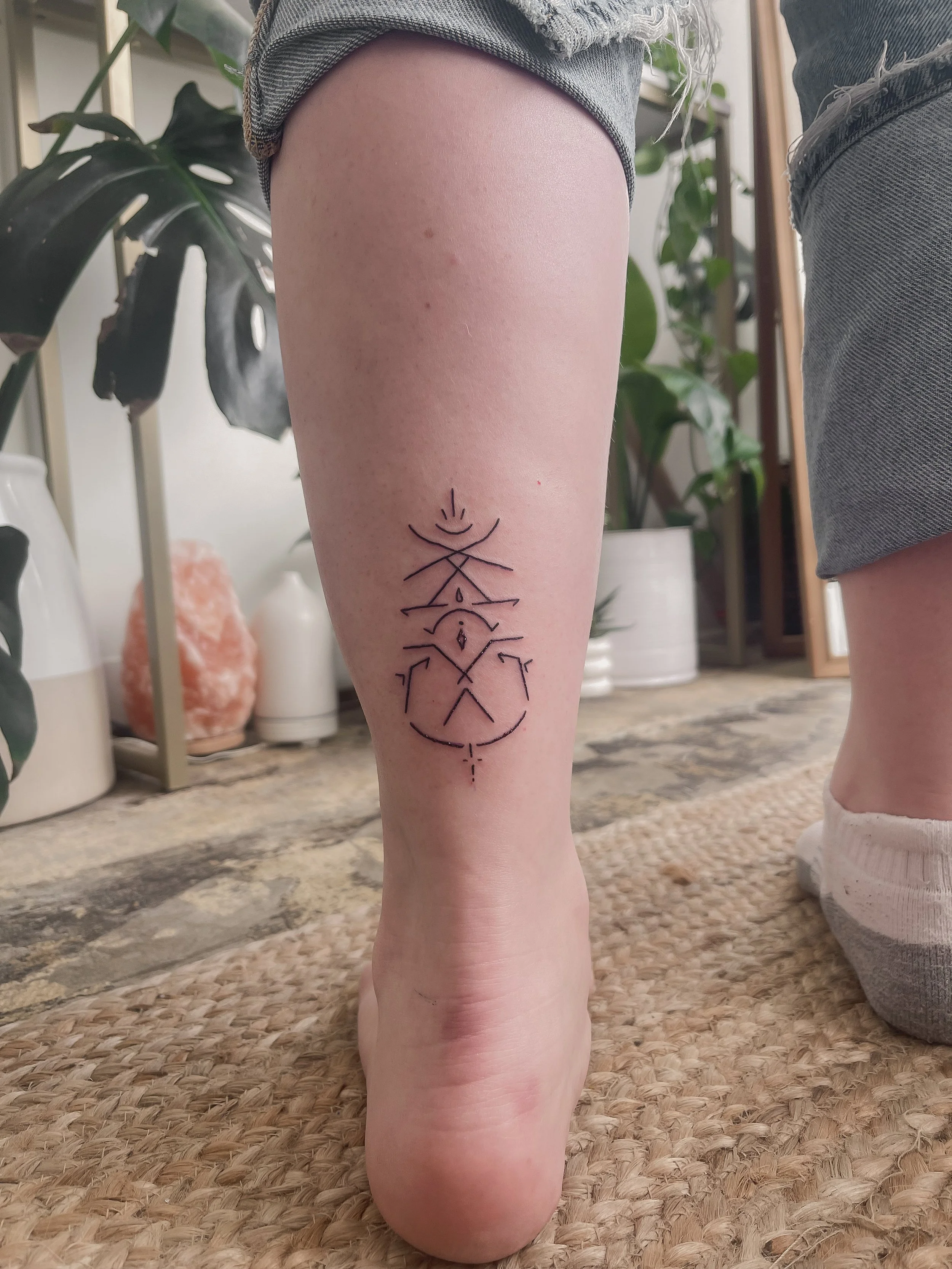 Tattoo of geometric and symbolic lines and shapes on a person's lower leg and ankle.