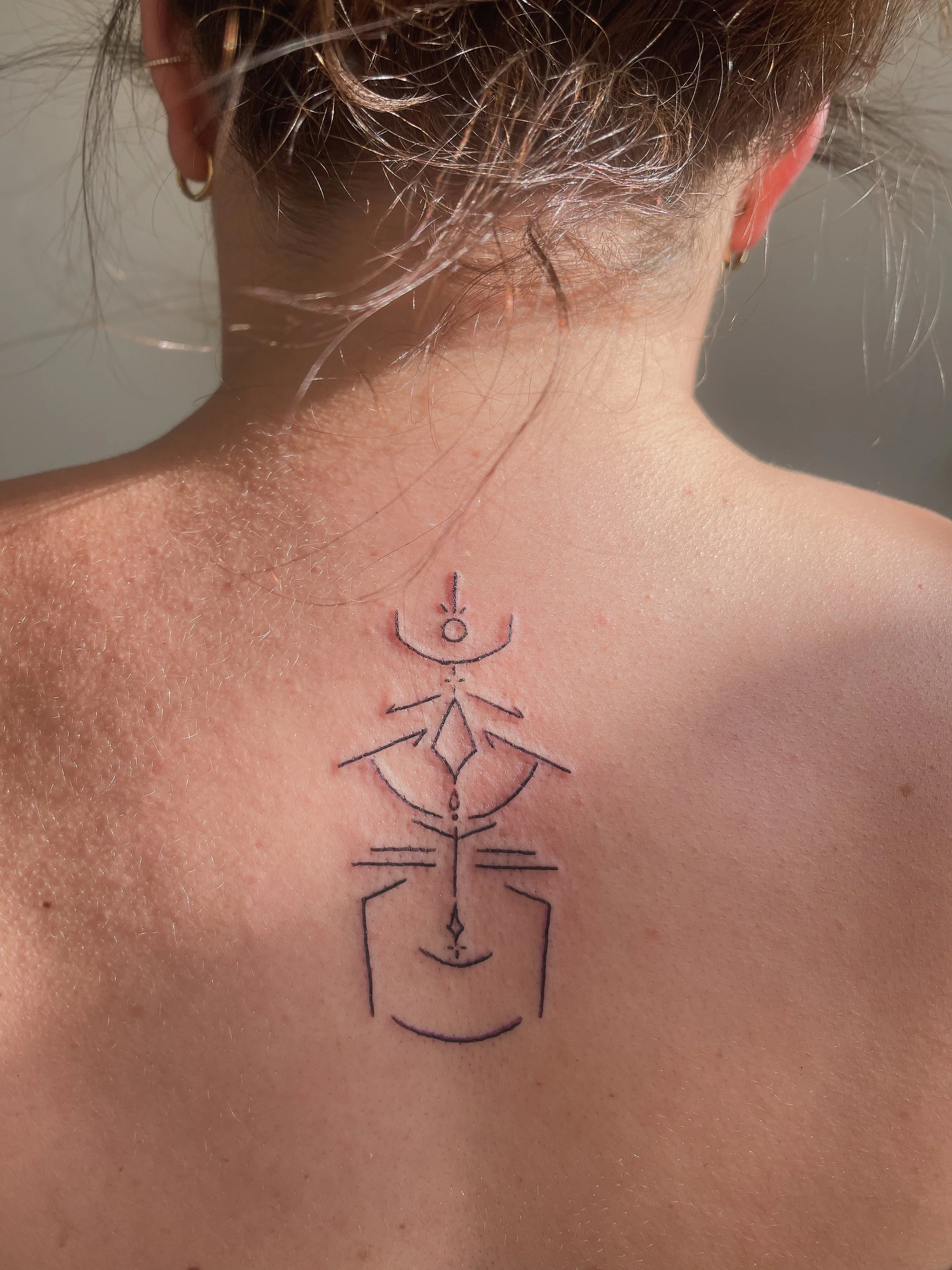 Tattoo of geometric and abstract symbols on person's upper back near the neck.