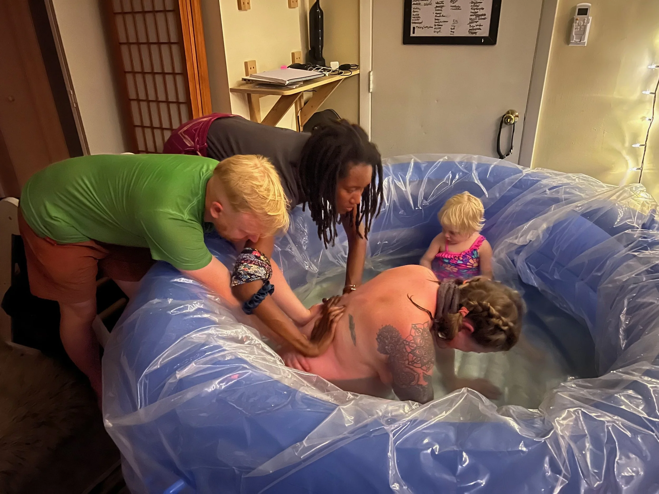 People participating in a water birth in an inflatable pool, with adults and children in a home setting.