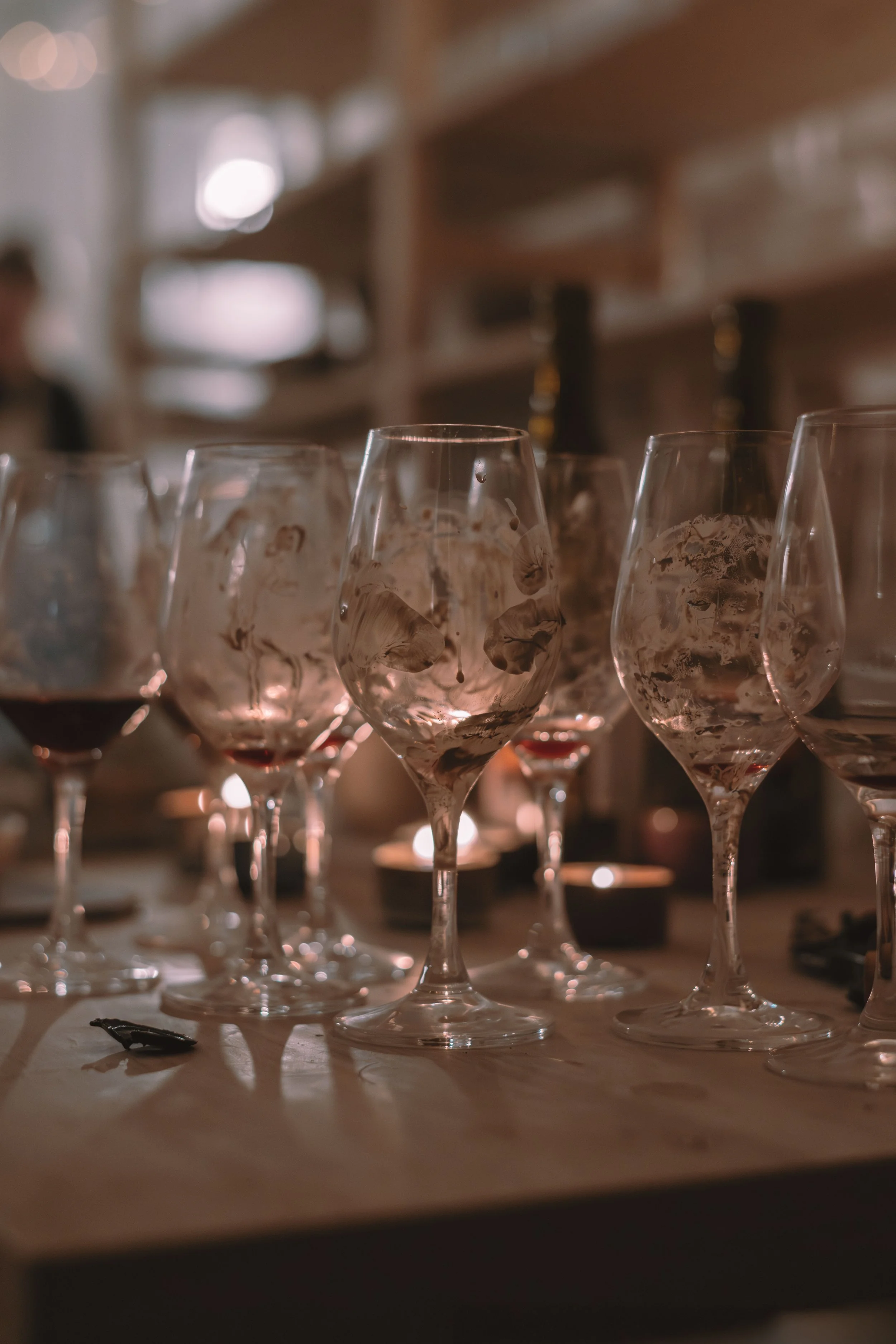 Several wine glasses, some with wine remnants, placed on a wooden surface in a softly lit room.