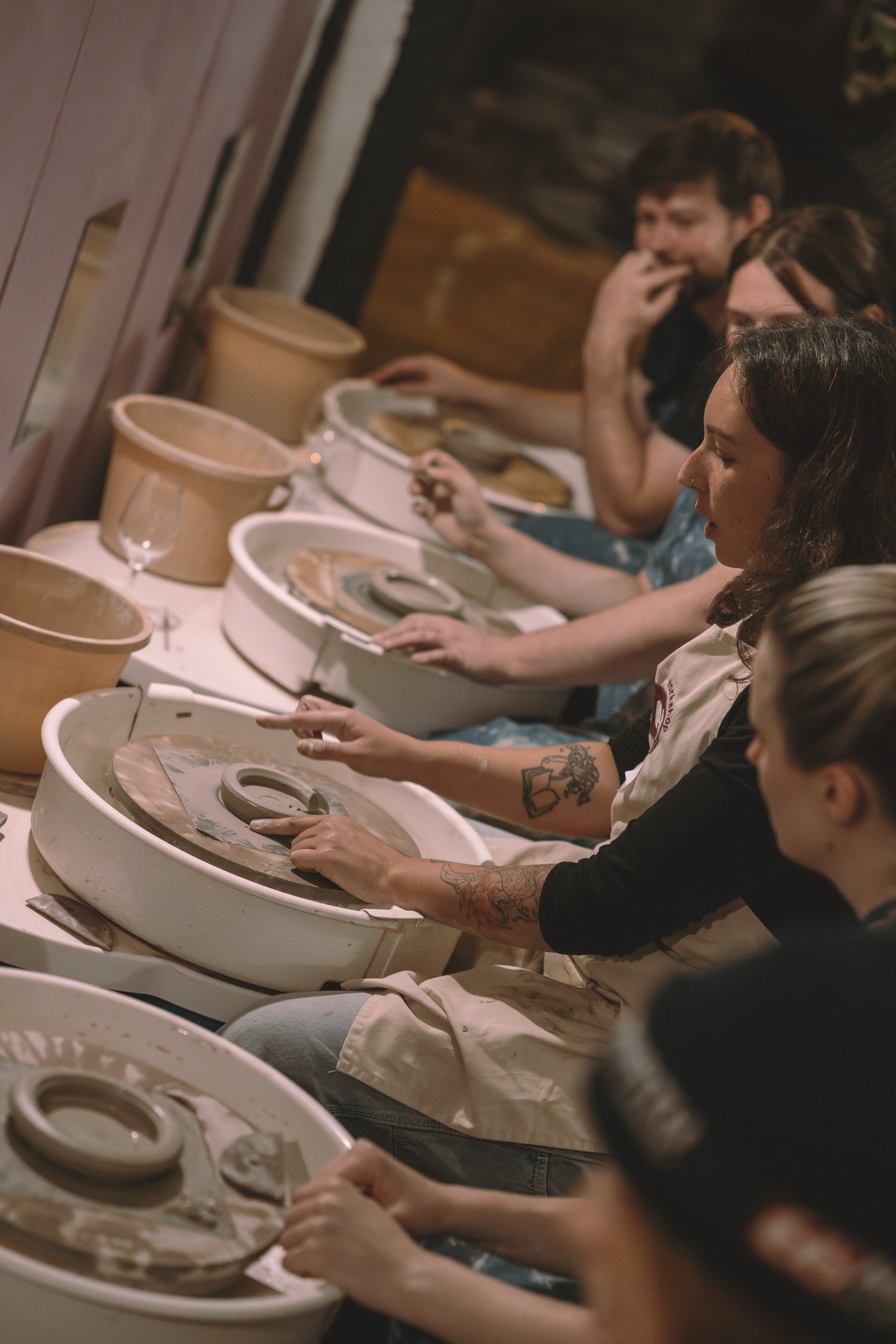 People sitting at a pottery wheel, shaping clay in a ceramics class.