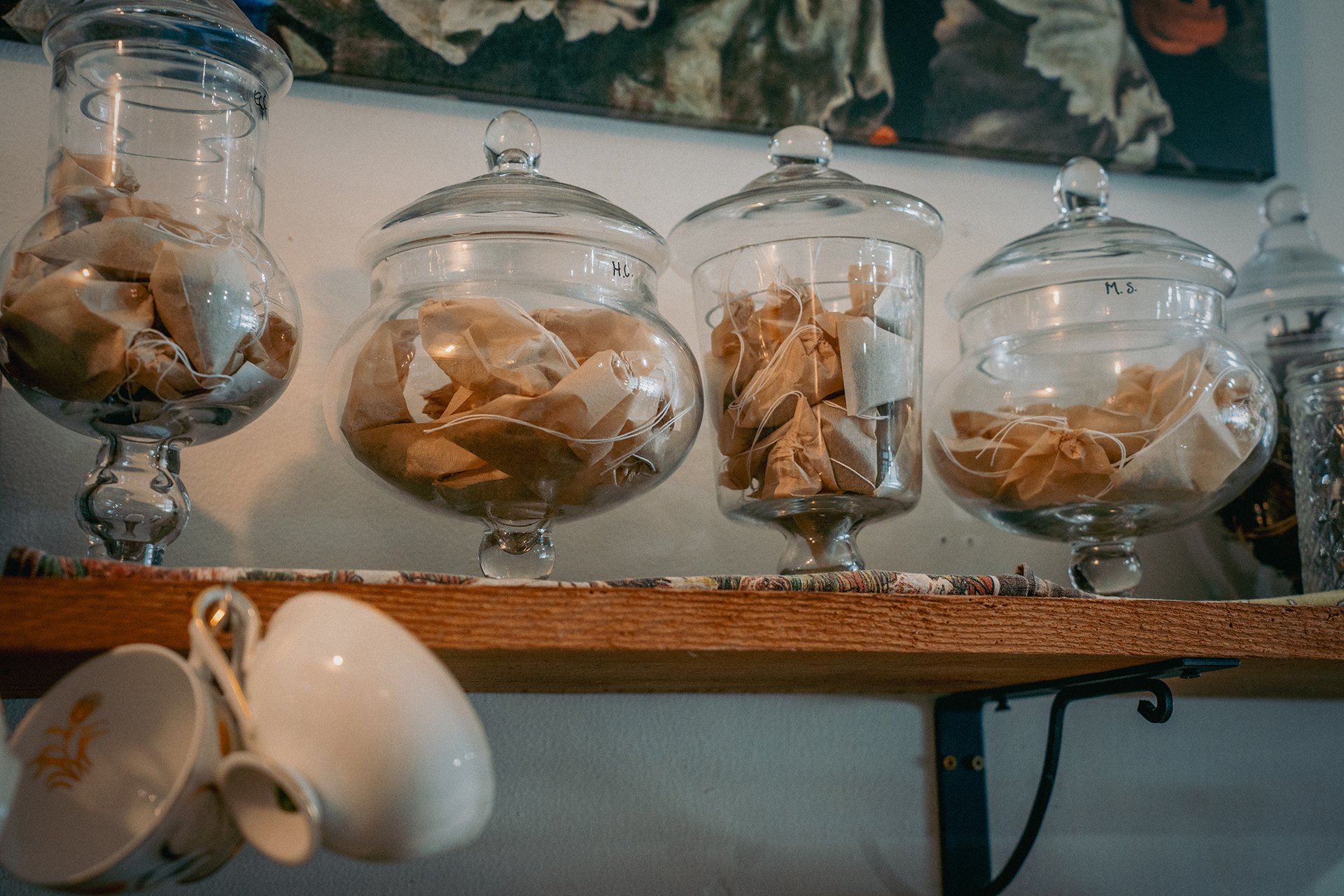 A display of glass jars holding custom-filled tea bags on a shelf at a cafe.