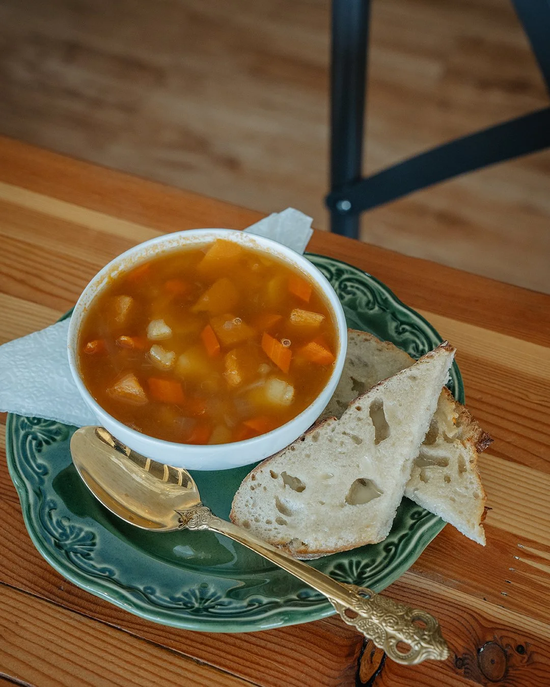 A bowl of vegetable soup with a spoon and toast sits on top of a table.