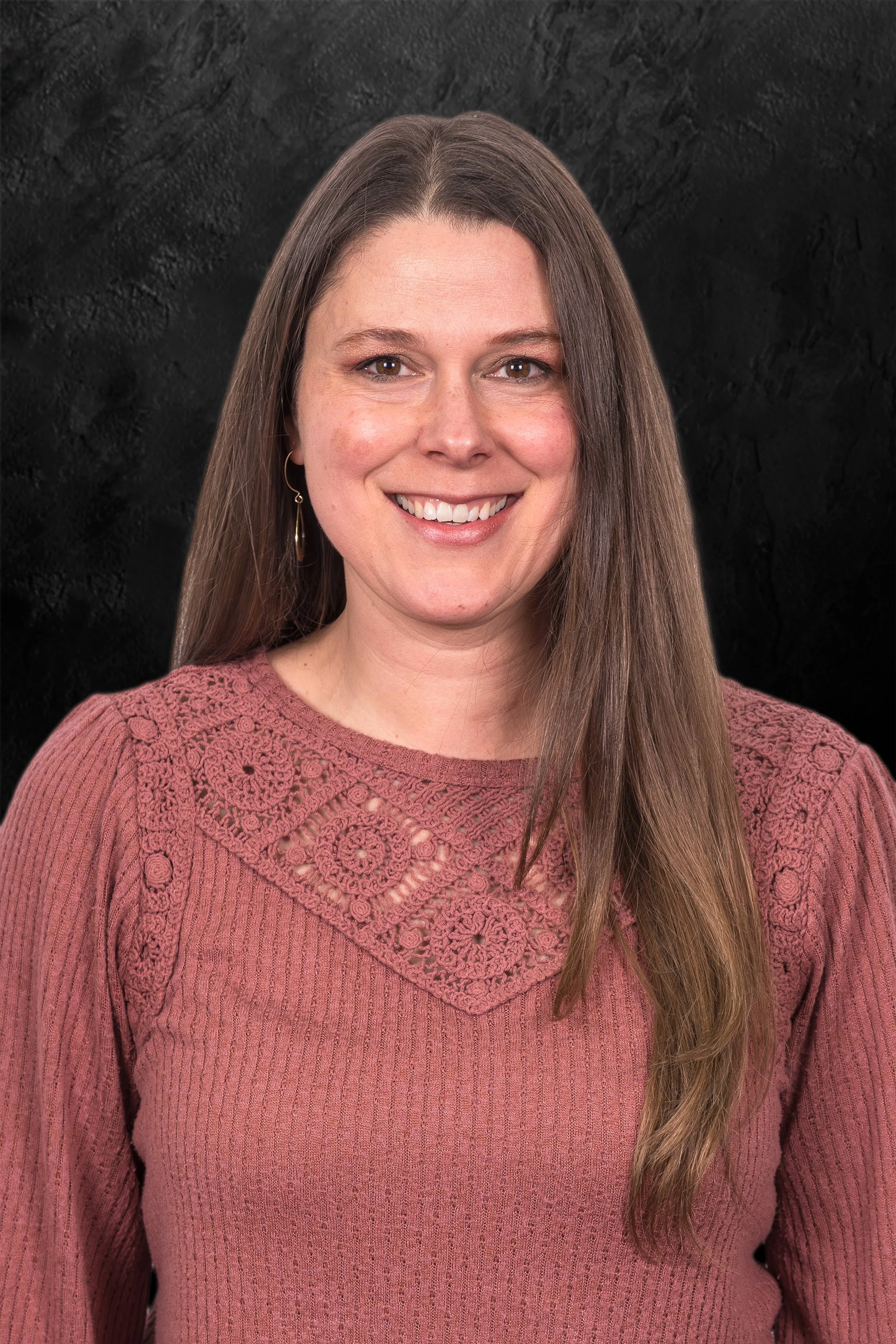 Smiling woman with long brown hair against a dark textured background.