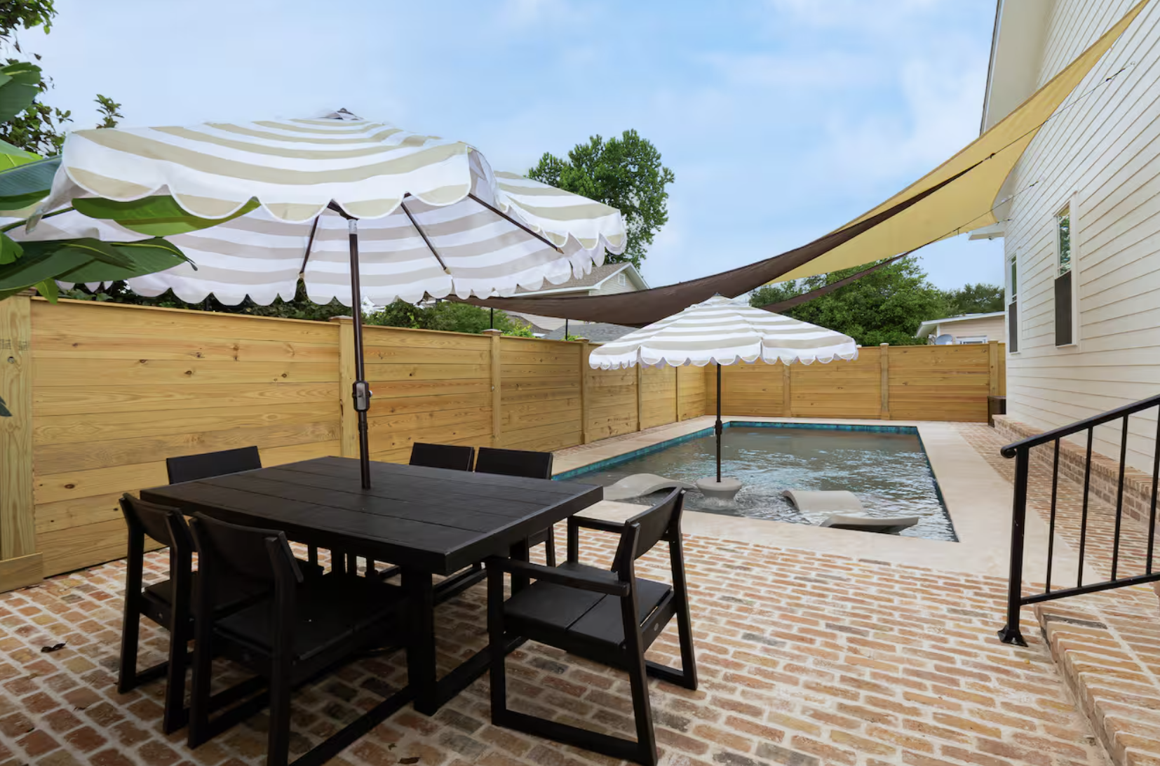 Pool surrounded by a brick patio with patio set and shaded sail over top.