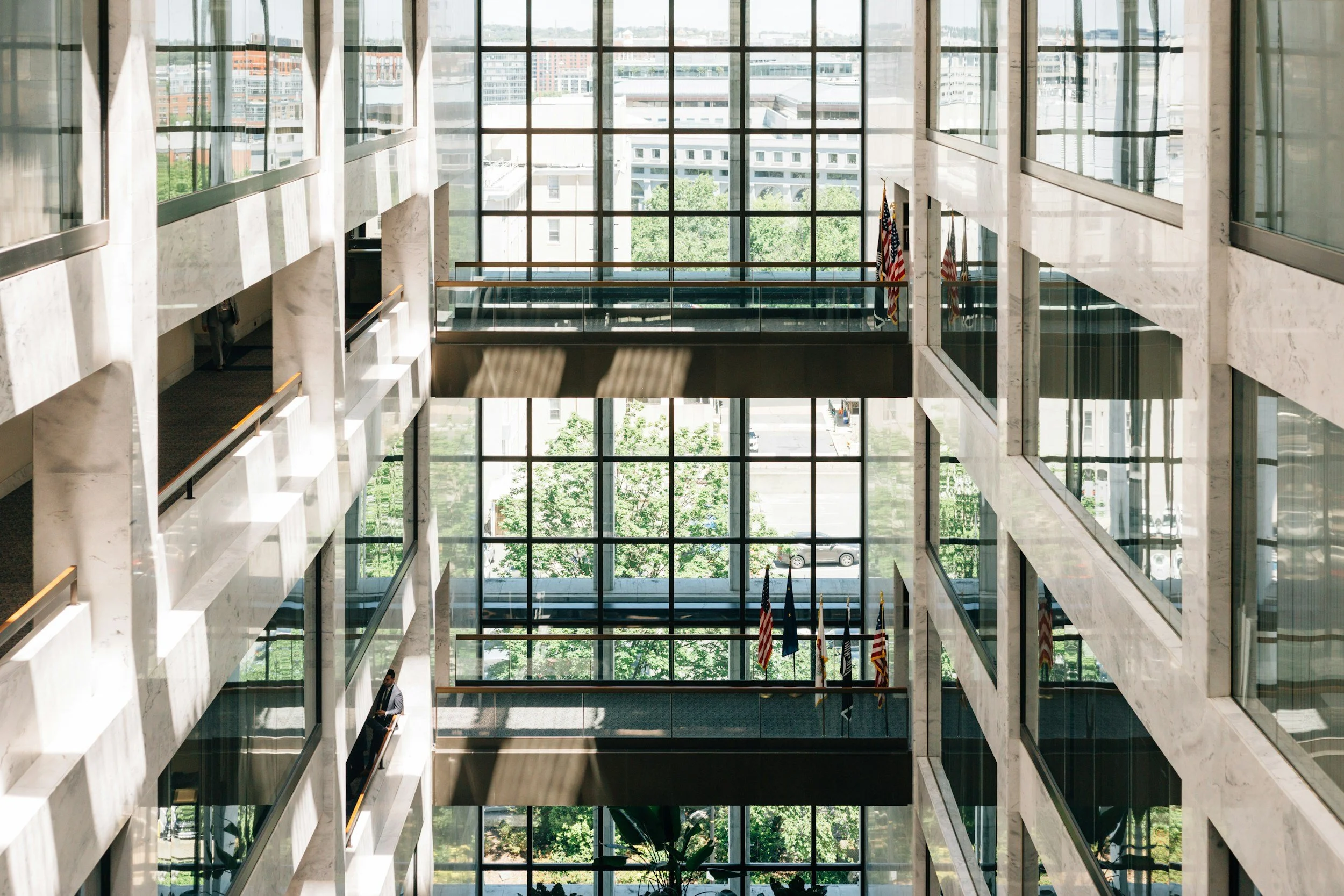Interior view of a modern office building atrium with large glass windows, multiple levels, and American flags.