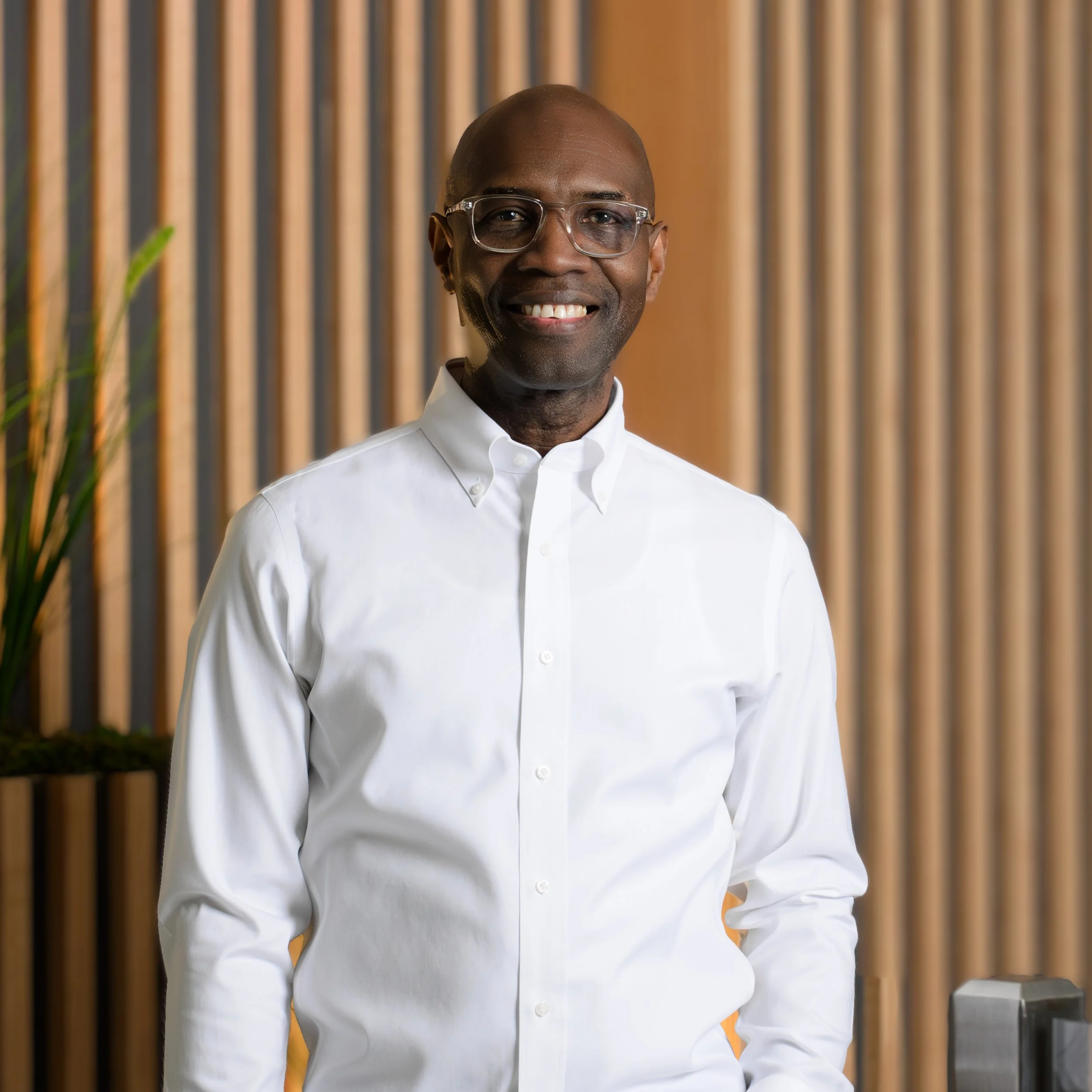 Man in a white button-up shirt smiling in front of a wooden slat background.