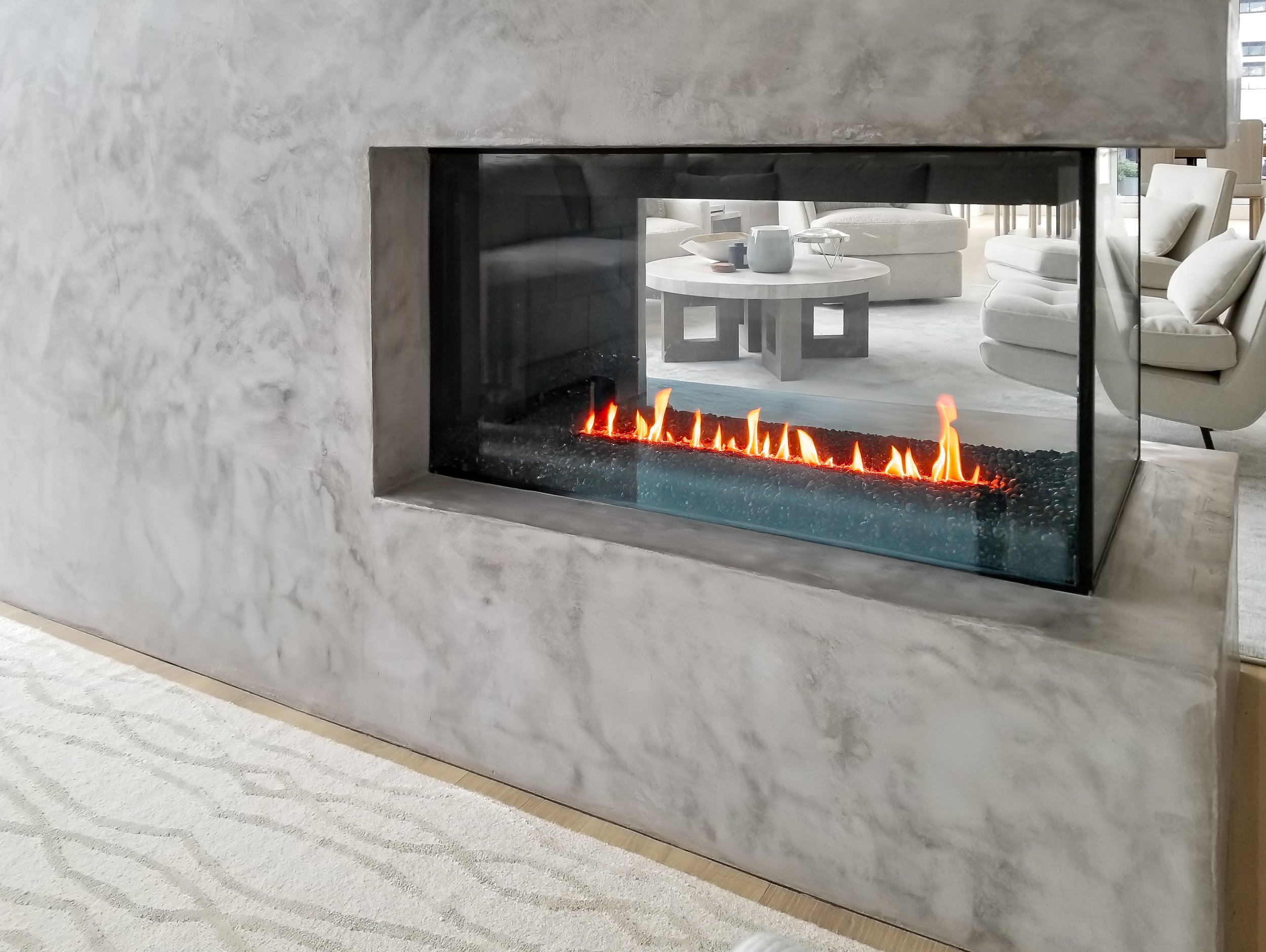 Modern gas fireplace in a marble-clad wall, with soft seating and a coffee table visible in the background.