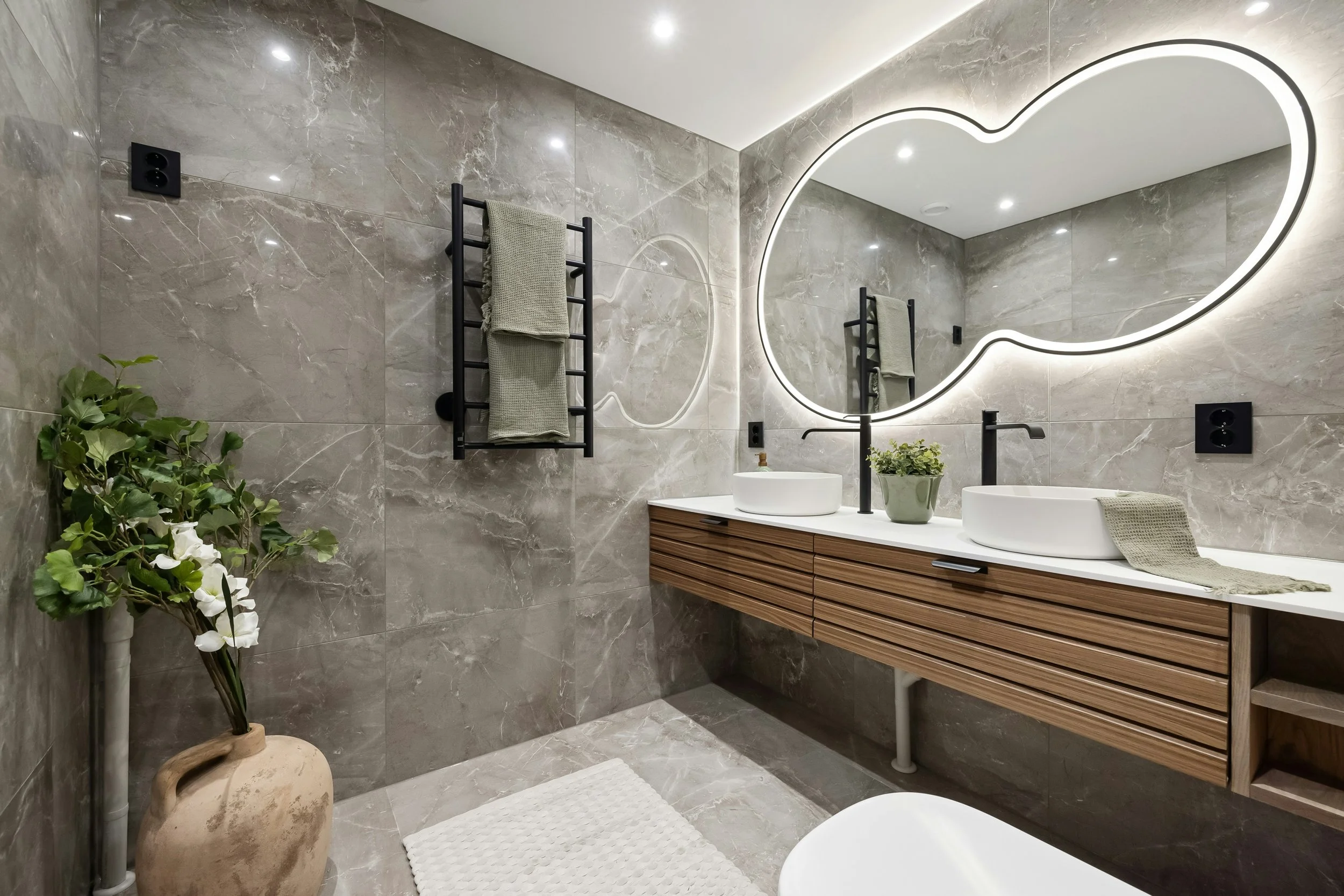 Modern bathroom with oval backlit mirror, wooden vanity with dual sinks, gray marble walls, towel rack, and decorative plants.