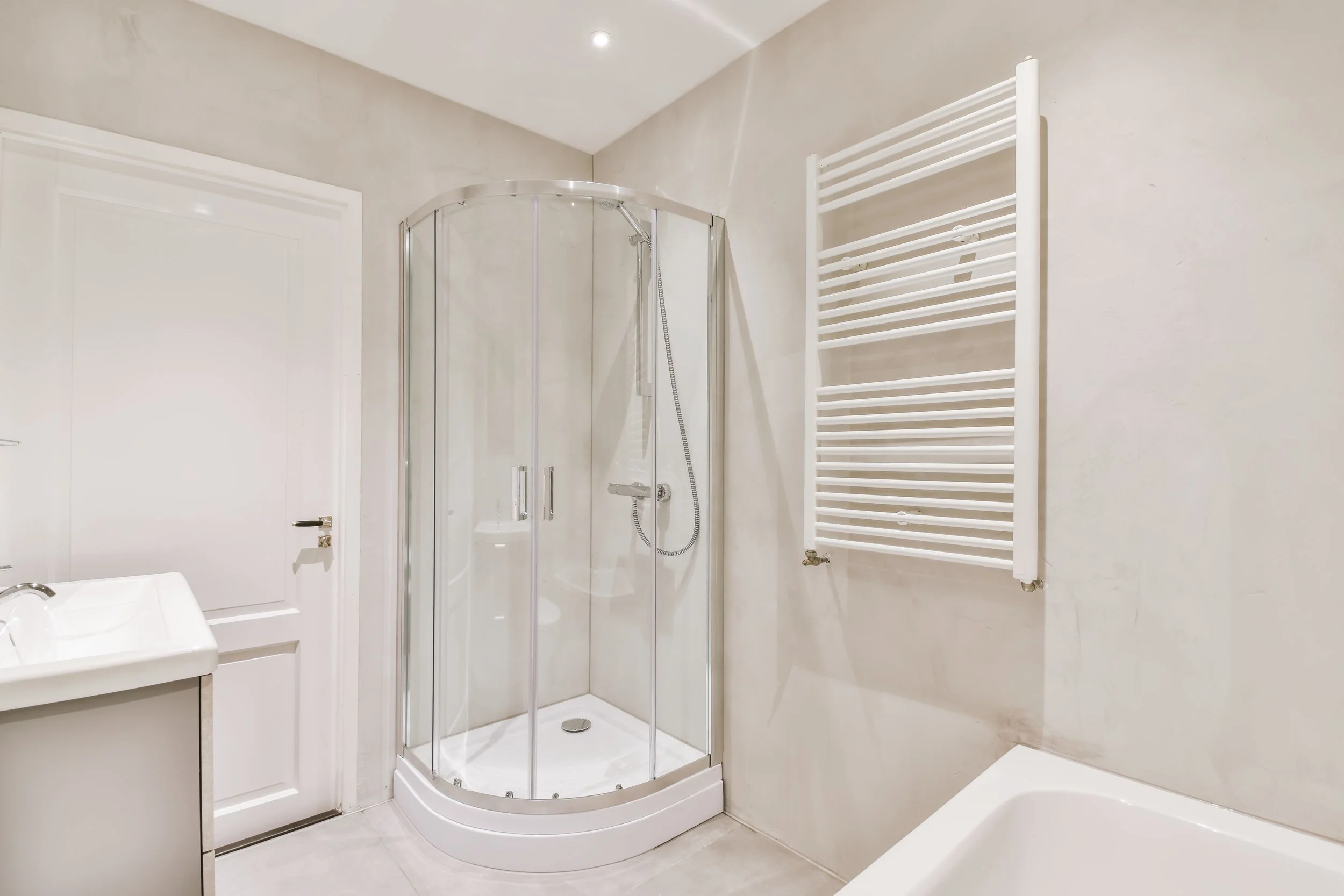 Modern bathroom with a glass-enclosed shower, white sink, towel warmer, and bathtub.