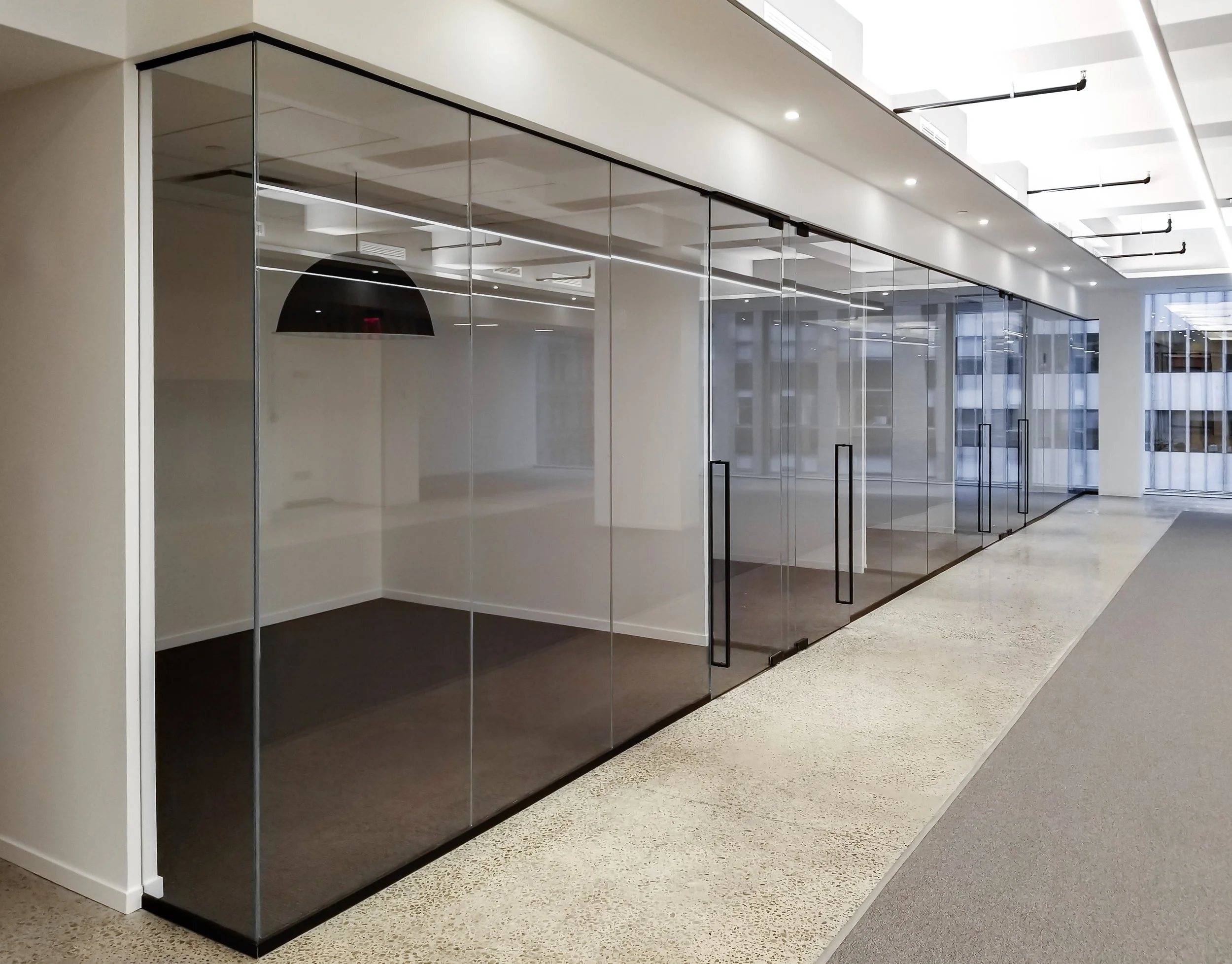 Modern office interior with glass walls and sliding doors, polished concrete flooring, recessed lighting, and a minimalist design aesthetic.