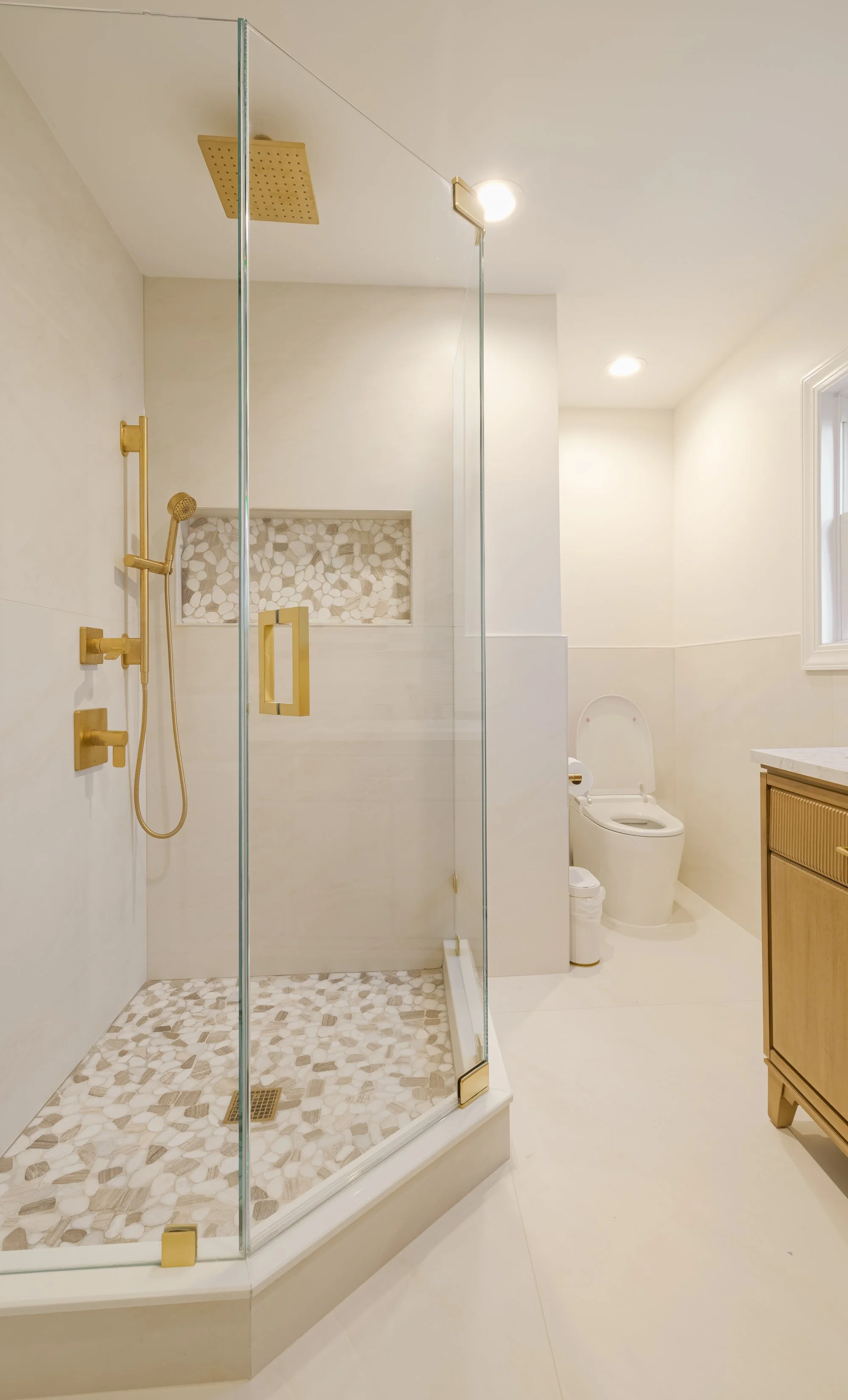 Modern bathroom with a glass shower, wooden vanity, black toilet, large mirror, gray textured walls, and tiled floor.