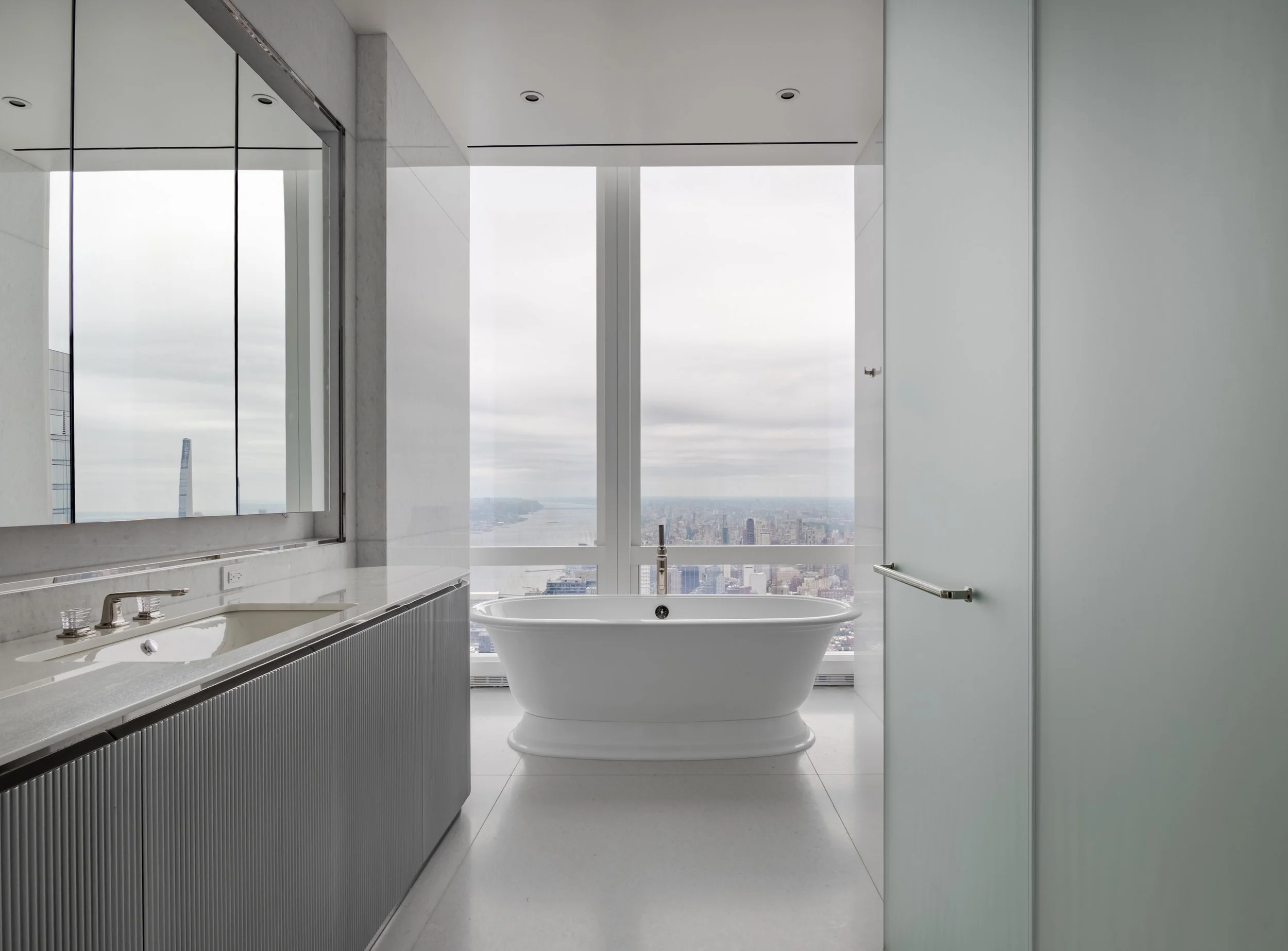 Modern bathroom with large windows, a freestanding bathtub, a sink with a mirror, and cityscape view.