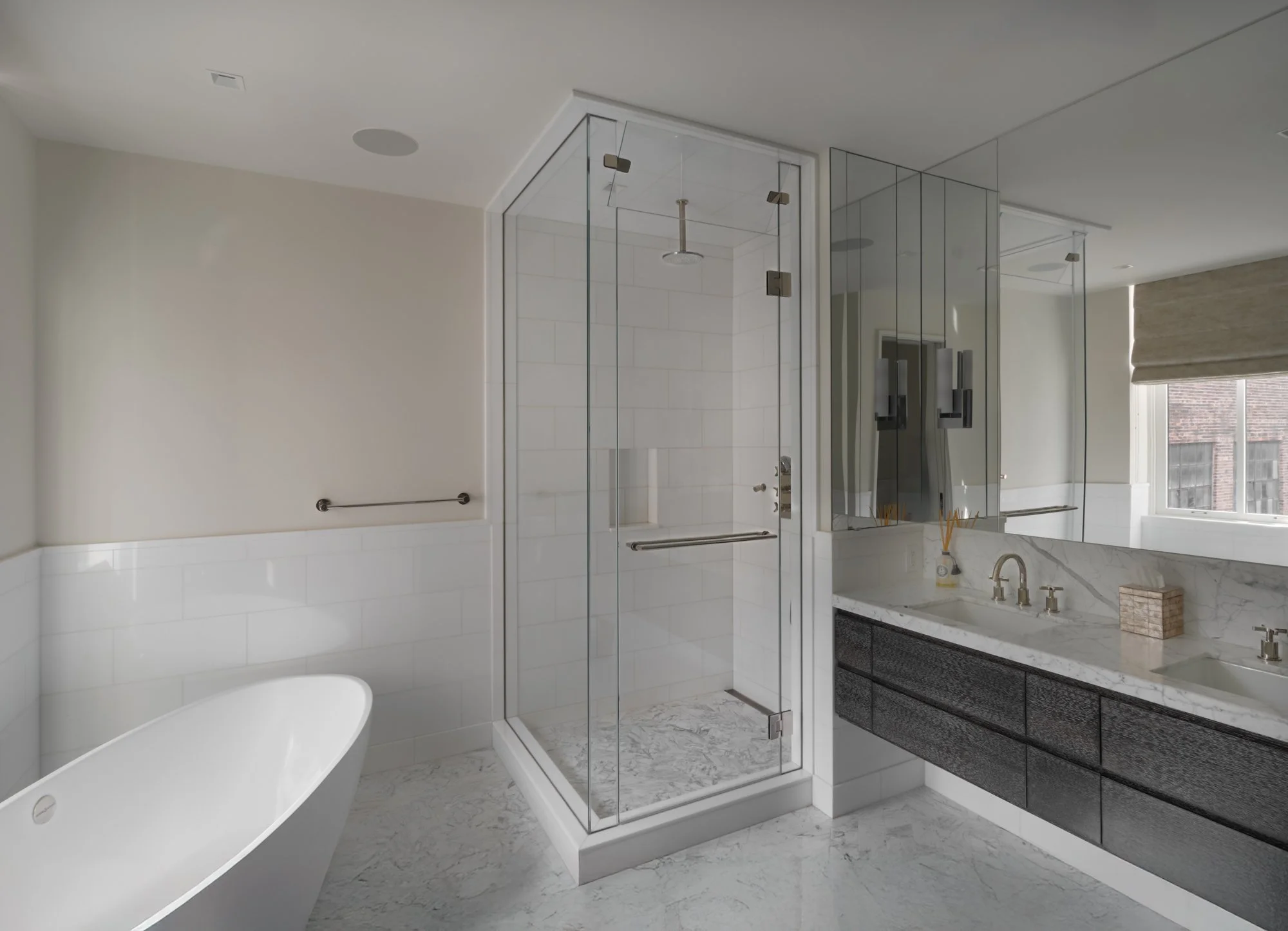 Modern bathroom with a glass shower enclosure and a toilet. The shower features a rain showerhead and a control panel on the smooth, light-colored wall. The floor is tiled, and the space is well-lit with recessed lighting.