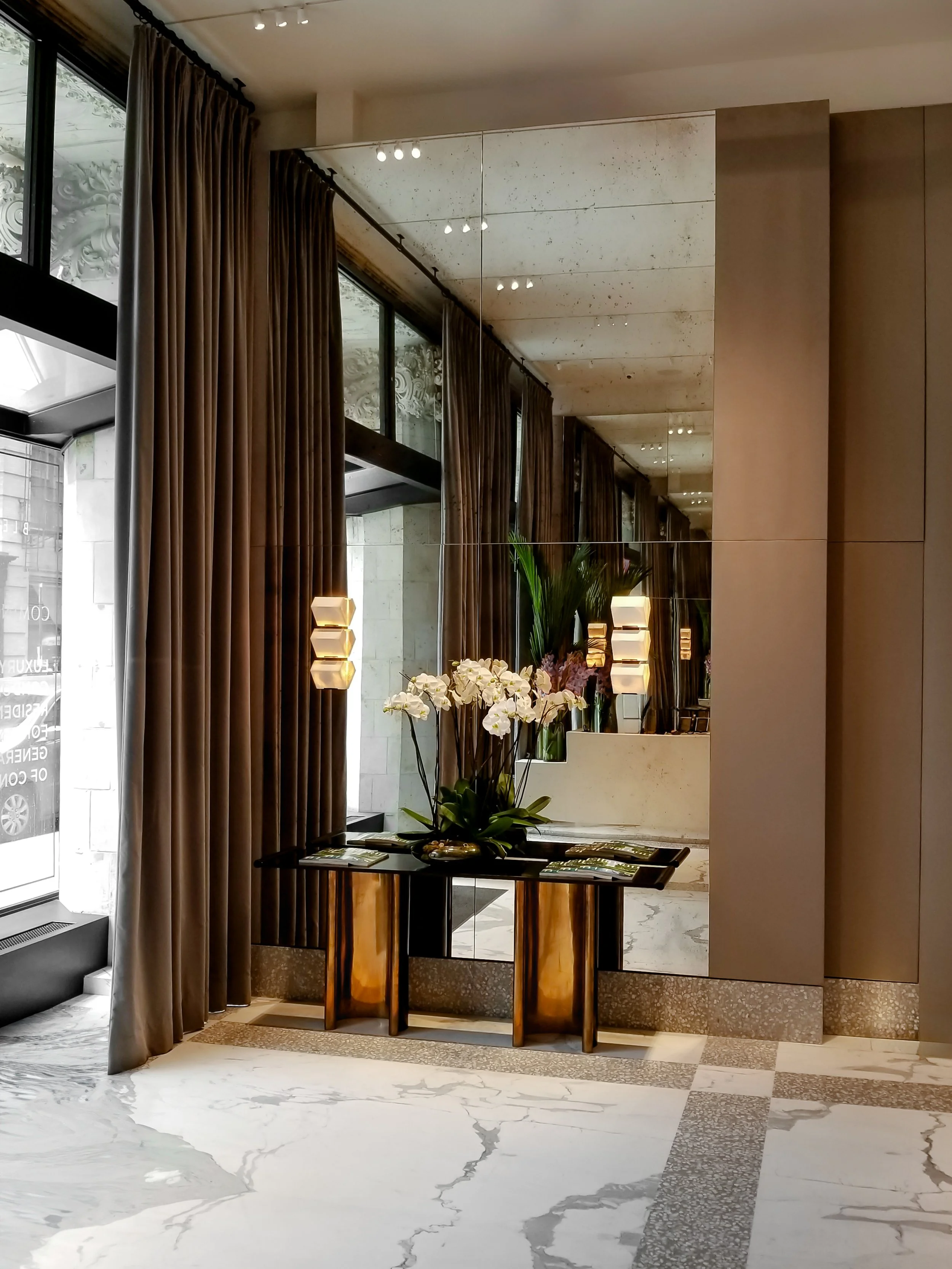 Elegant interior with a mirrored wall, brown curtains, and a black console table decorated with white orchids.