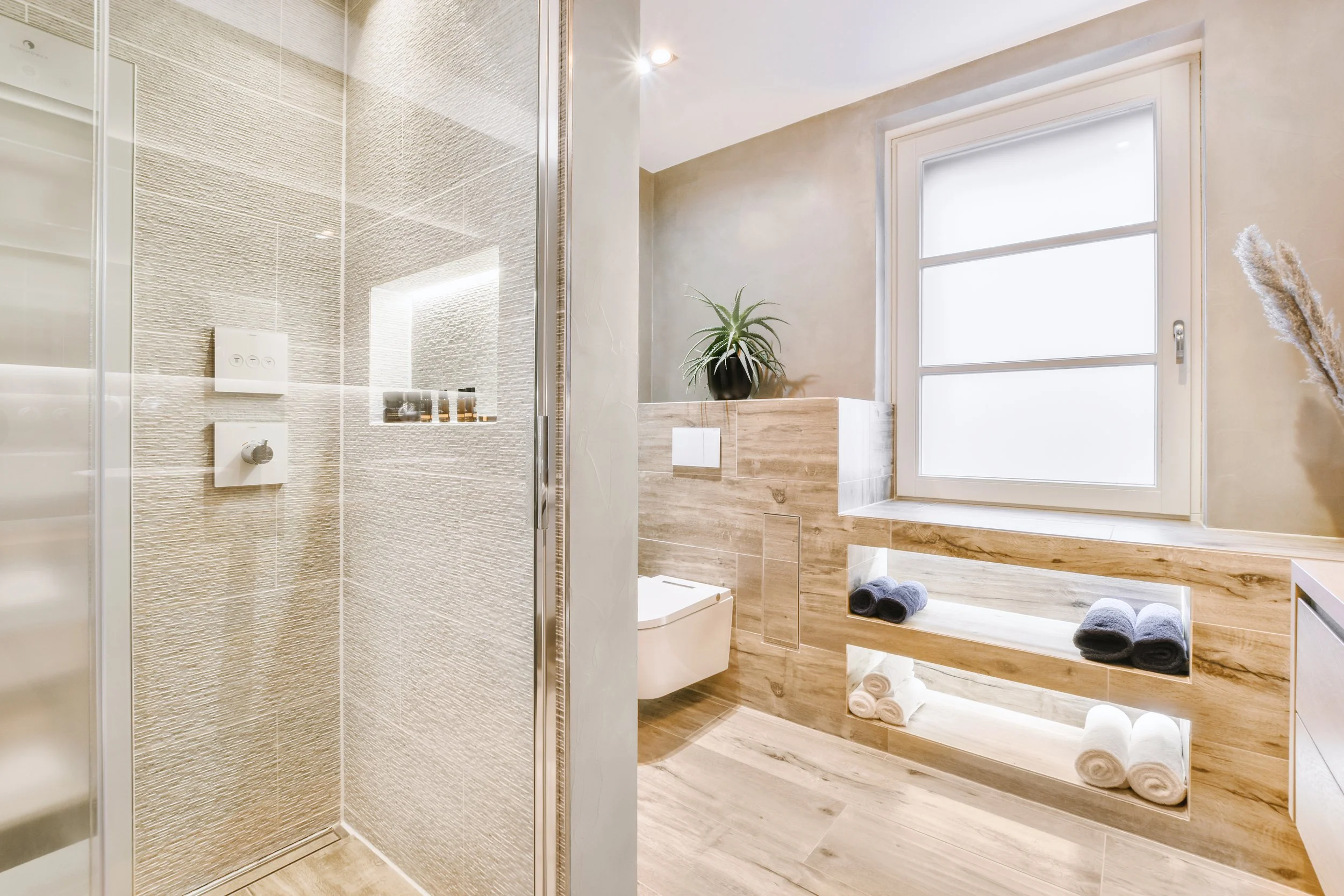 Modern bathroom with glass shower, wooden accents, window, shelves with towels, and a potted plant.