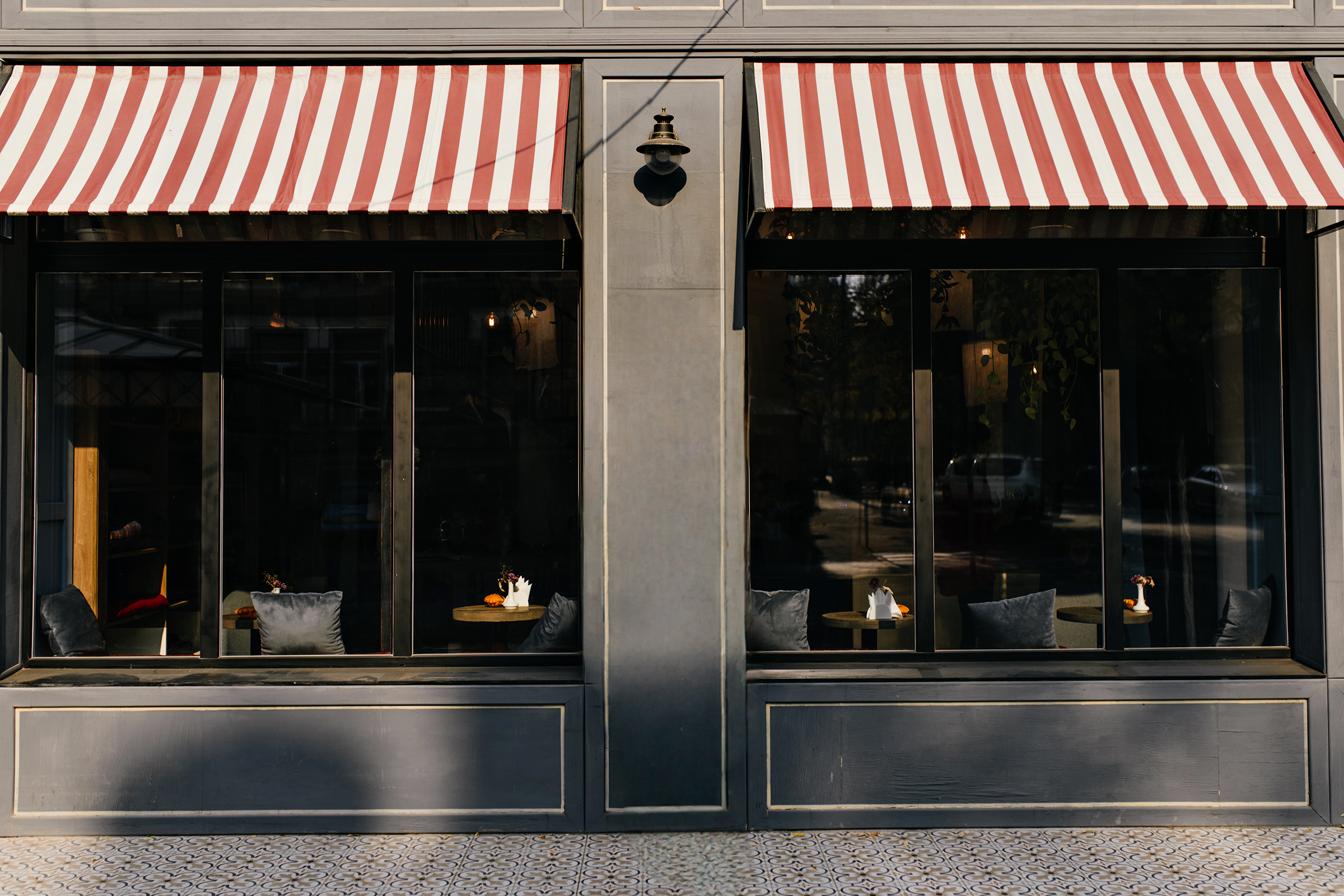 Exterior of a cafe with striped awnings and large windows, framed storefront, showing tables and chairs inside.
