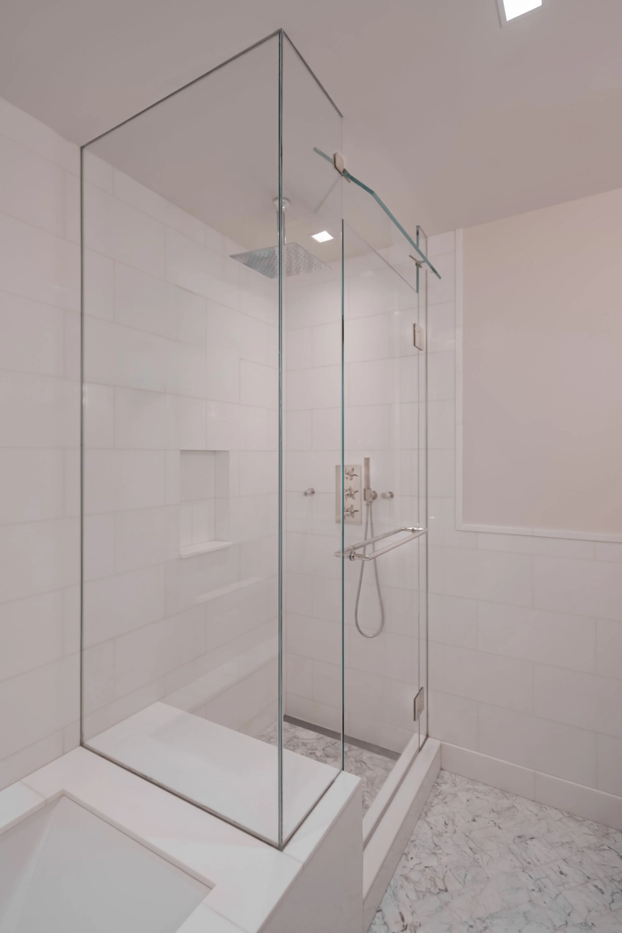 Modern glass-enclosed shower with white subway tiles and silver hardware.