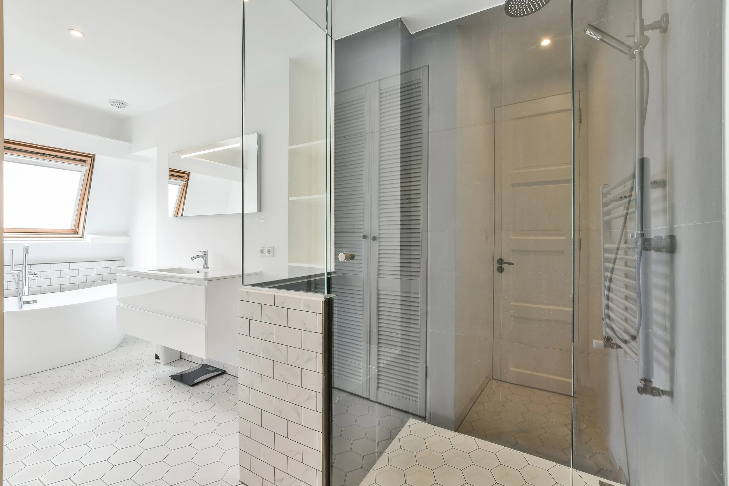 Modern white bathroom with glass shower, hexagonal floor tiles, vanity, and a skylight.