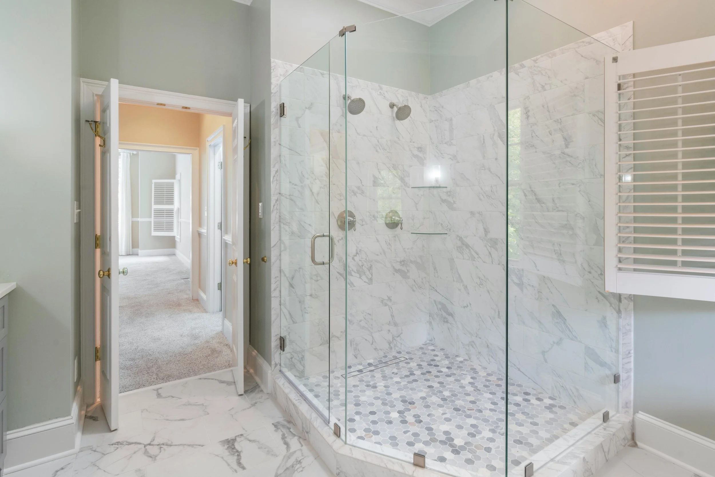 Bathroom with glass-enclosed marble shower and open door leading to carpeted hallway.