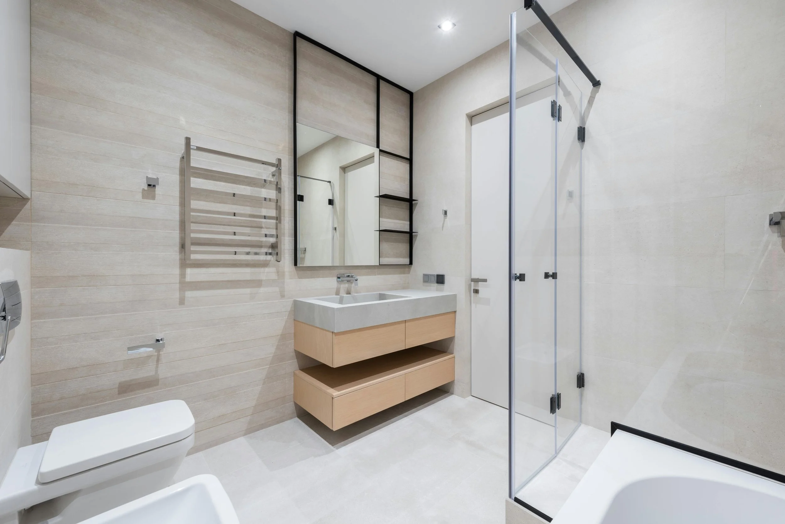 Modern bathroom with wall-mounted sink, floating cabinets, glass shower enclosure, towel rack, toilet, and large mirror.