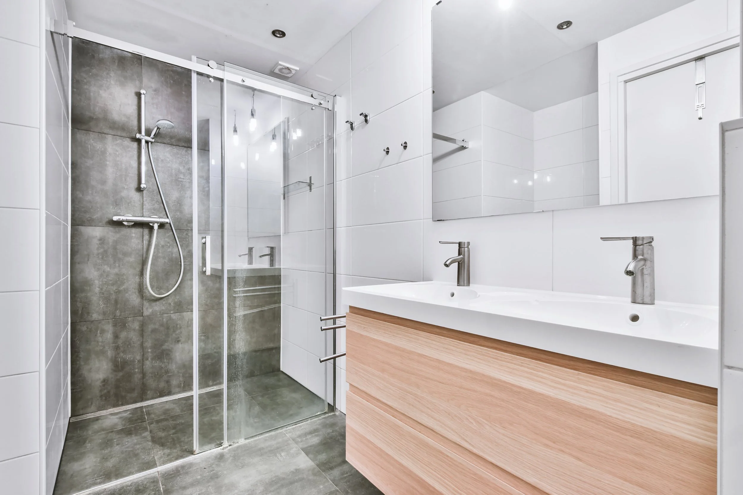Modern bathroom with glass shower enclosure, gray tiles, and wooden vanity with dual sinks.