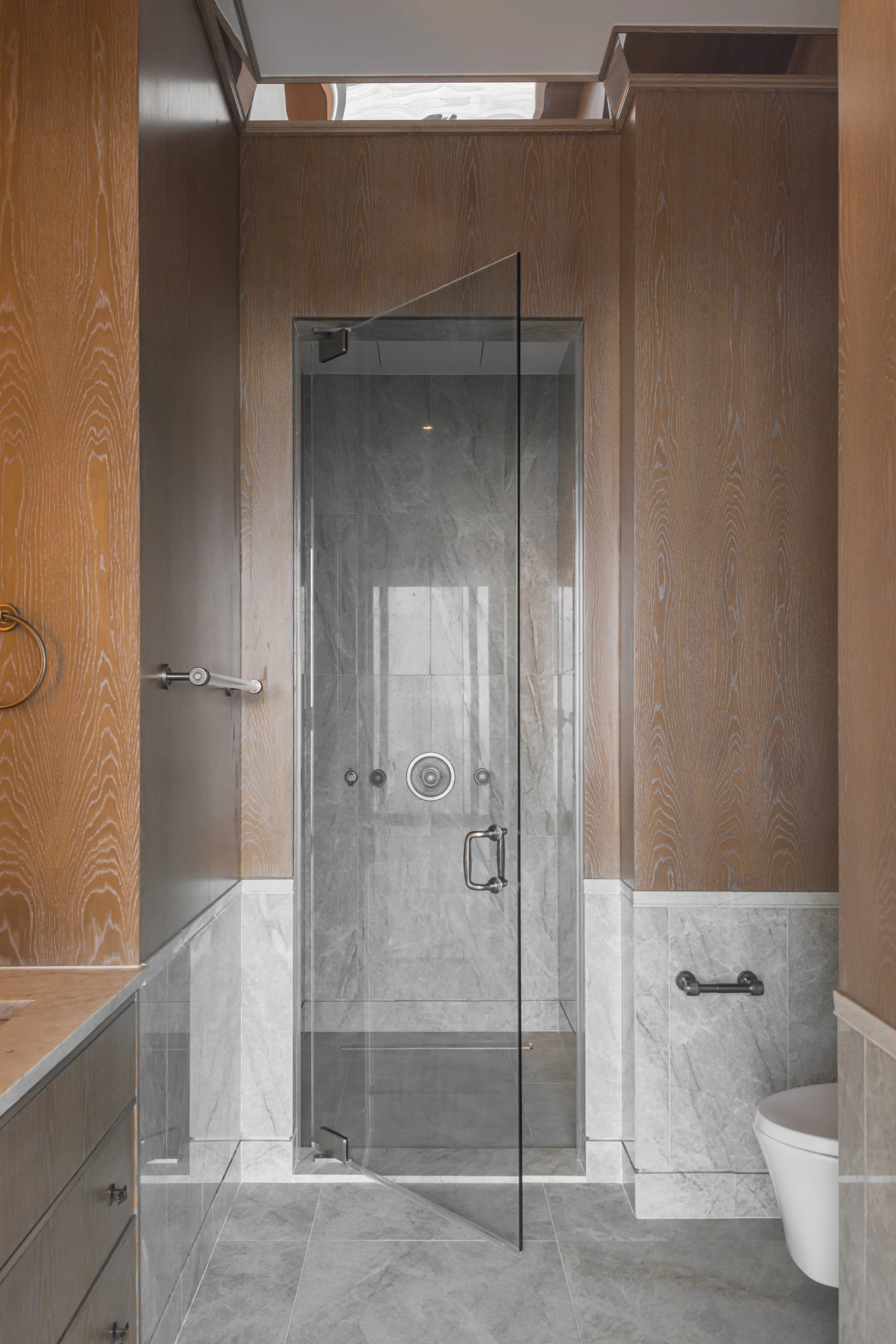 Luxurious marble bathroom with a glass shower door, golden showerhead, and elegant wall tiles.
