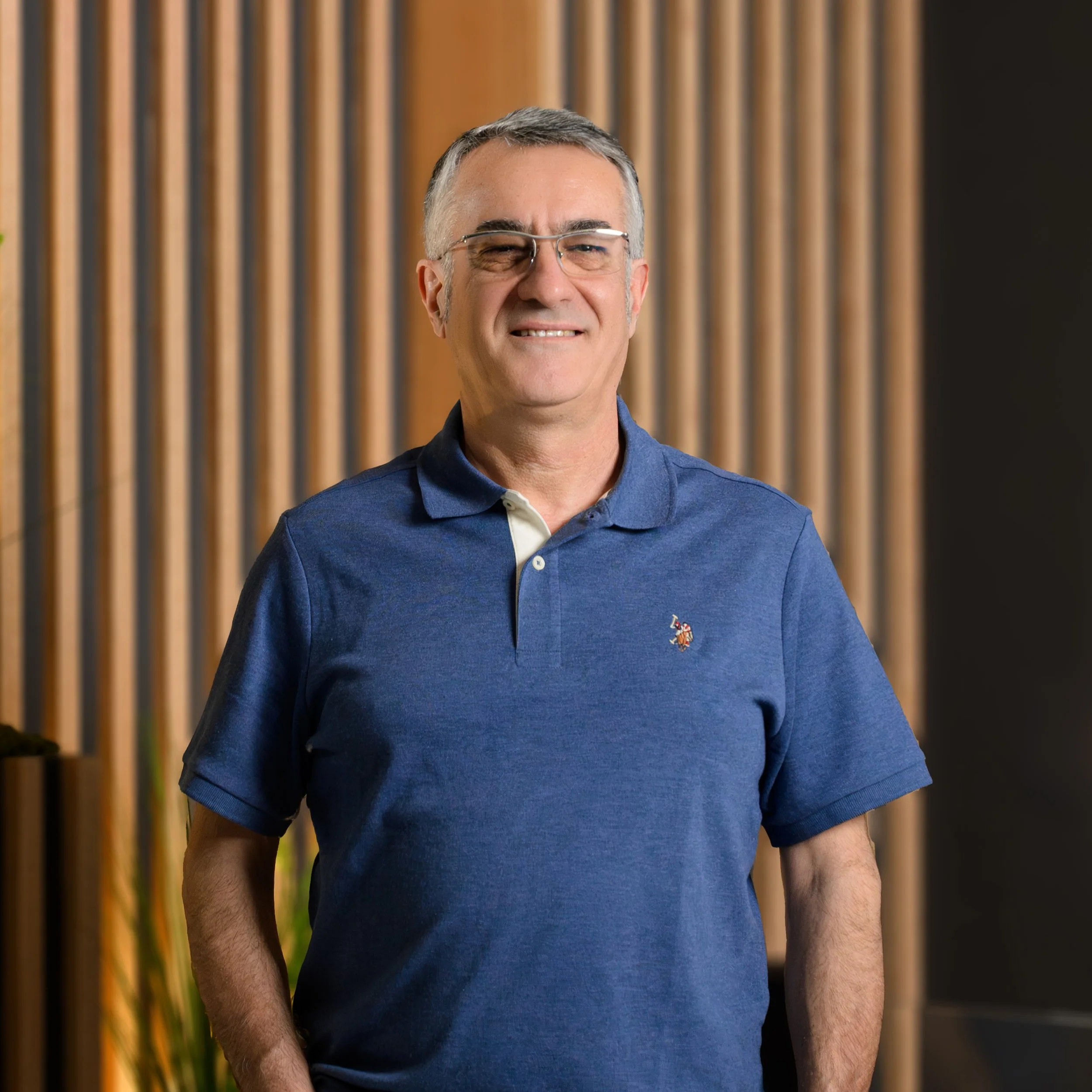 Man in blue polo shirt standing in front of a wooden panel background.