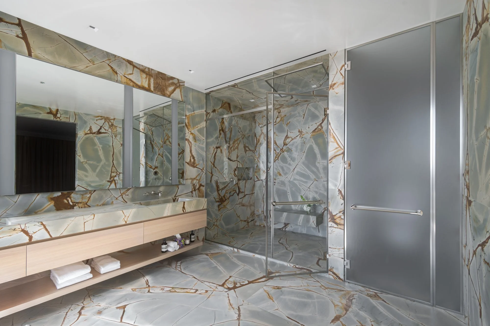 Modern bathroom with glass-enclosed marble shower and freestanding bathtub.