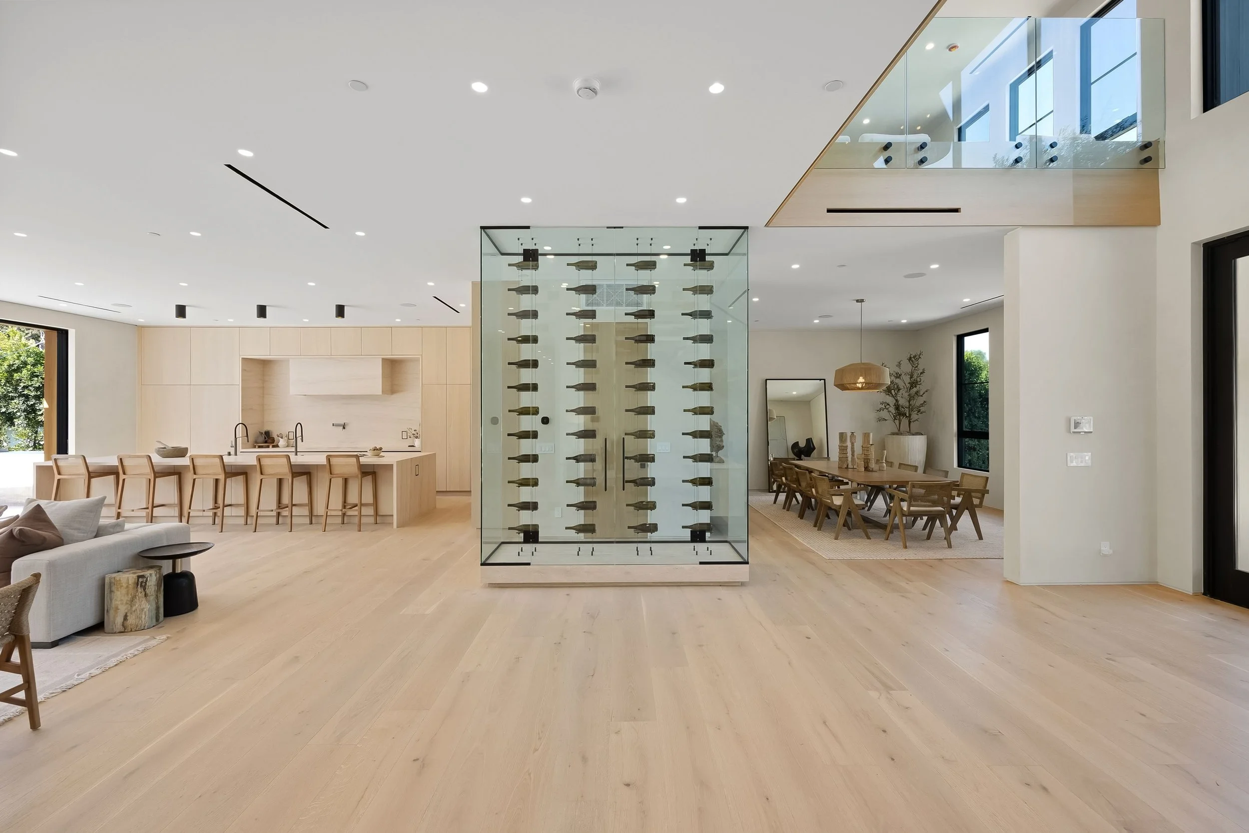 Modern open-plan kitchen and dining room with wooden flooring, glass wine storage, and natural light.