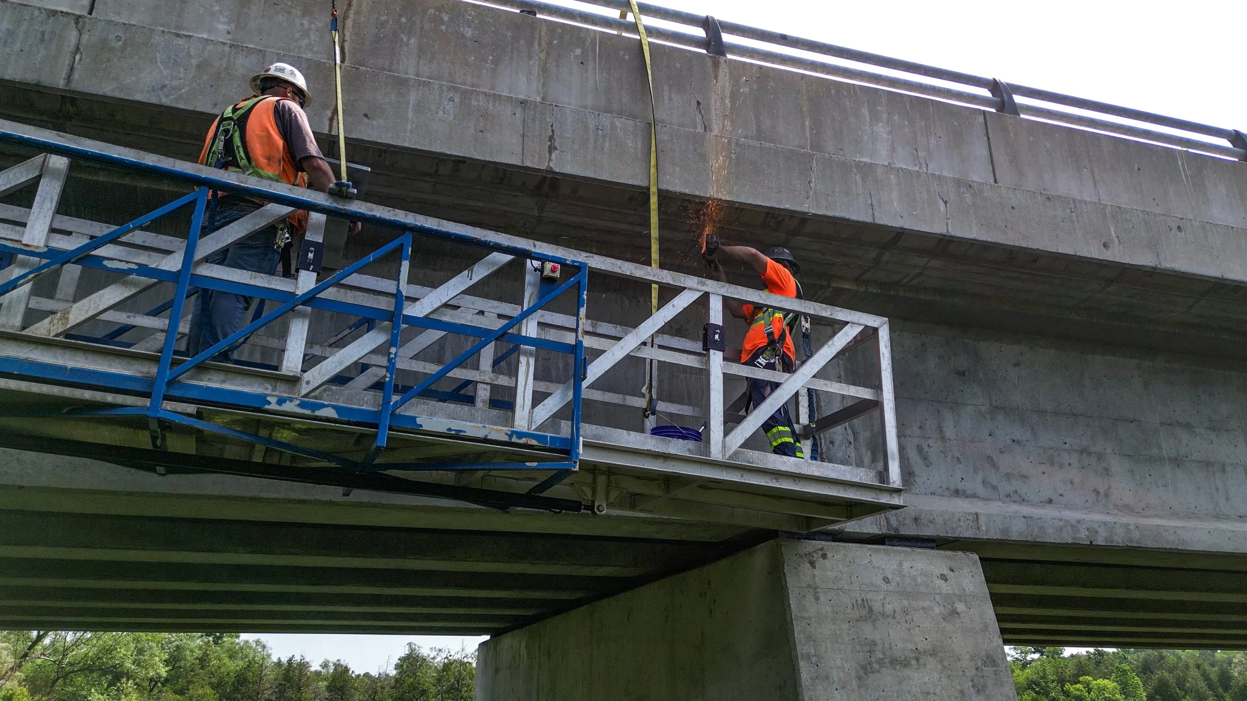 Construction workers wearing safety gear working on a bridge underpass, using scaffolding and welding equipment.