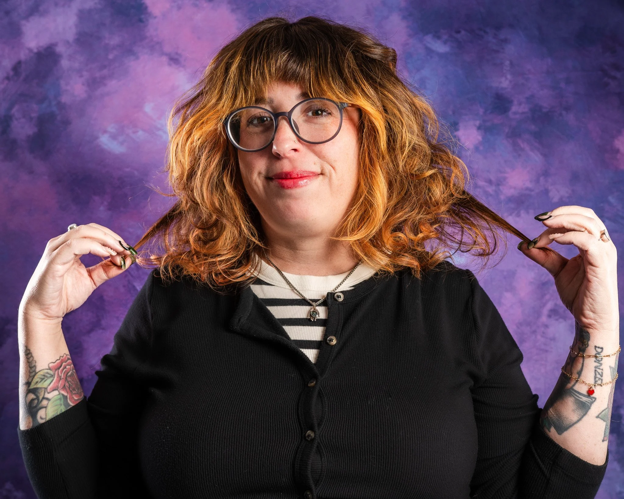 Headshot client for beauty studio smiling and holding her hair with both hands against a purple, textured background.