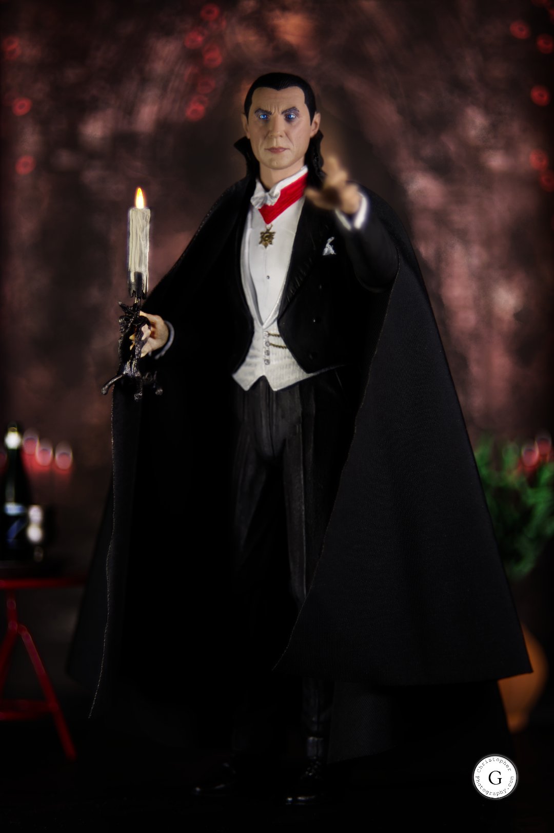 A detailed figure of Dracula in a black cape, white shirt, and red cravat, holding a lit candle, with a dark, blurred background.
