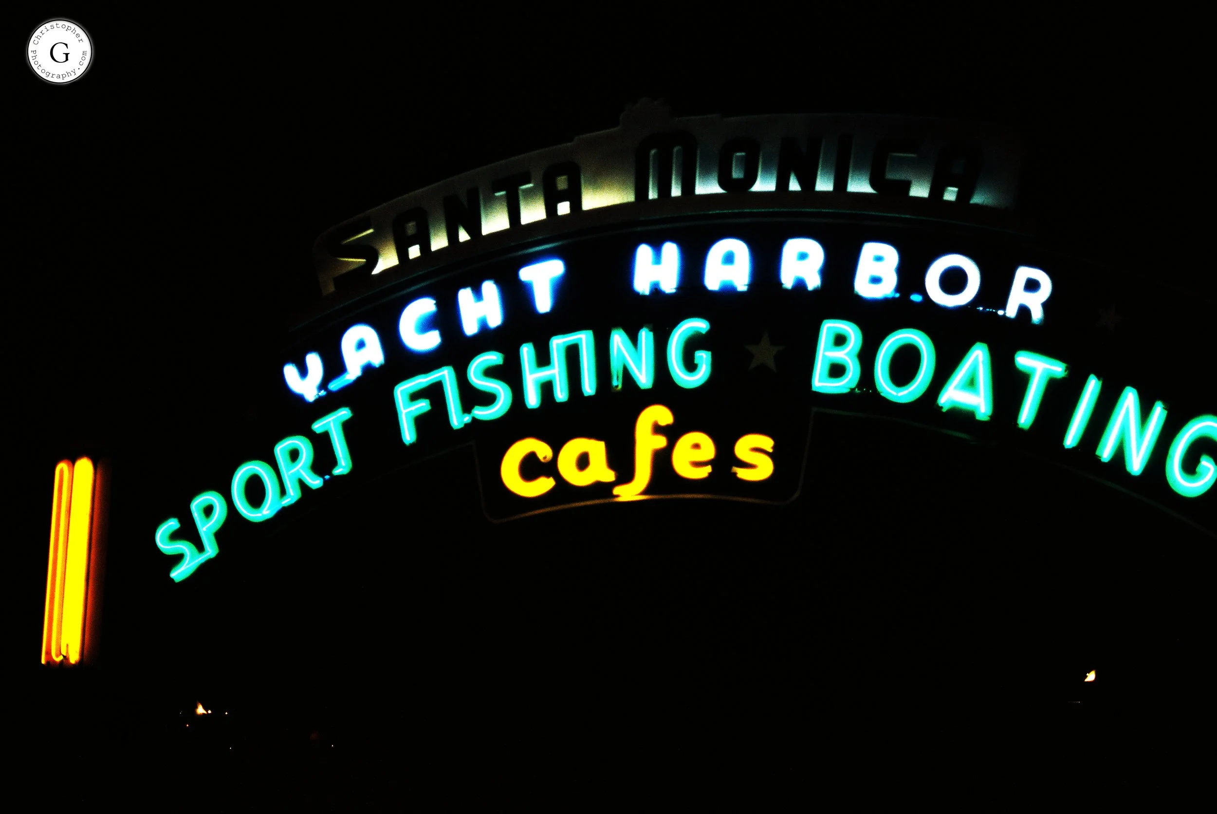 Neon sign for Santa Monica, California, advertising a yacht harbor, sport fishing, boating, and cafes, against a dark night sky shot on 35mm film .