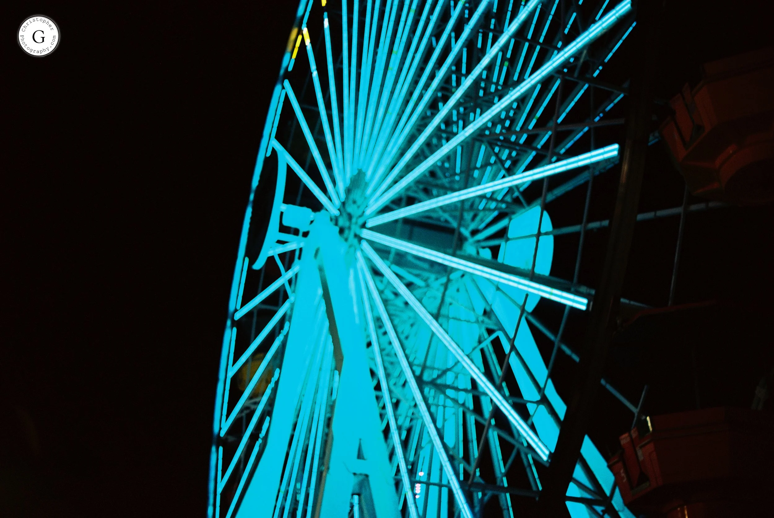 A brightly lit Ferris wheel at night with blue neon lights shot on 35mm film.