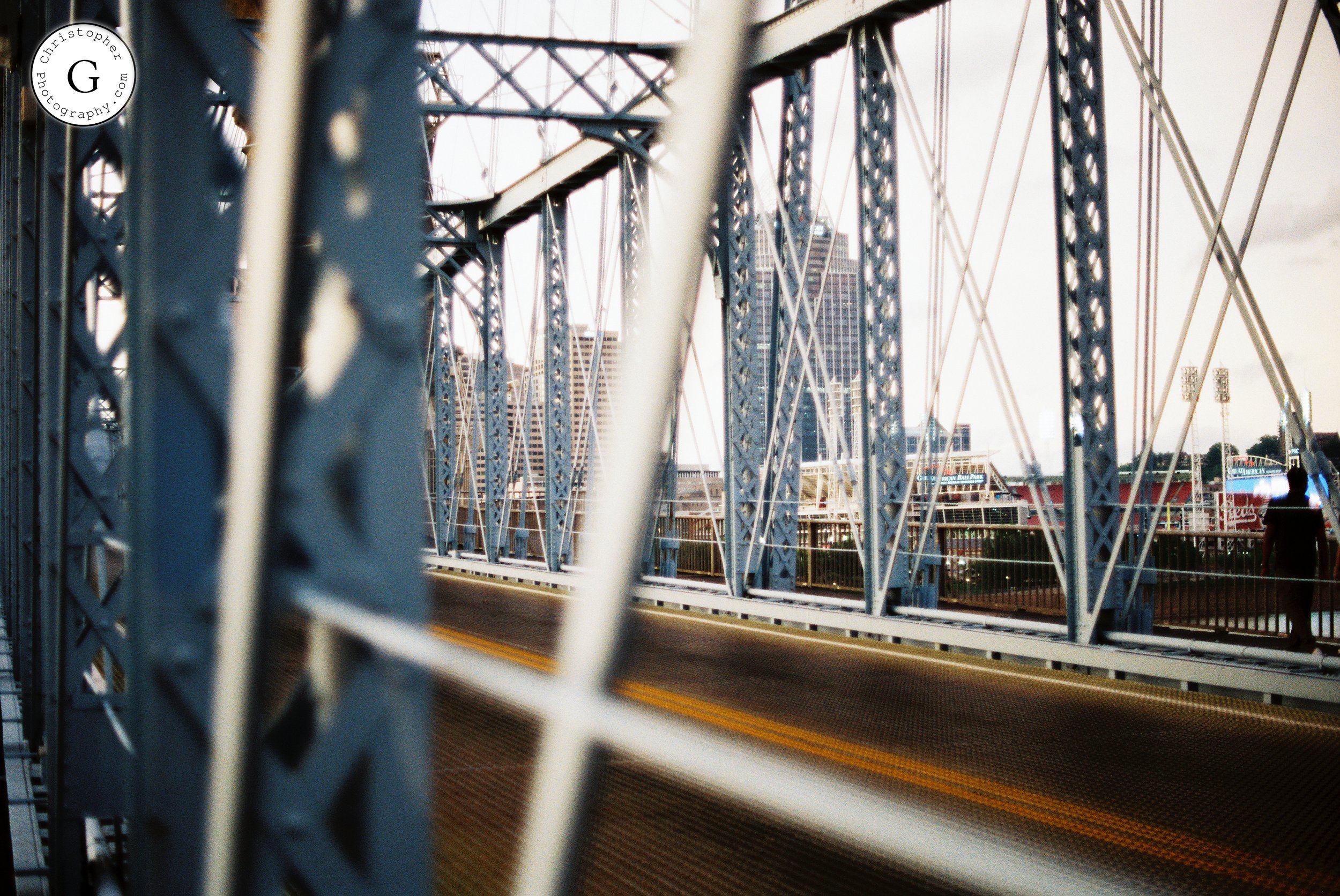 Close-up view of the cables and metal framework of a bridge with buildings and a person in the background shot on 35mm film .