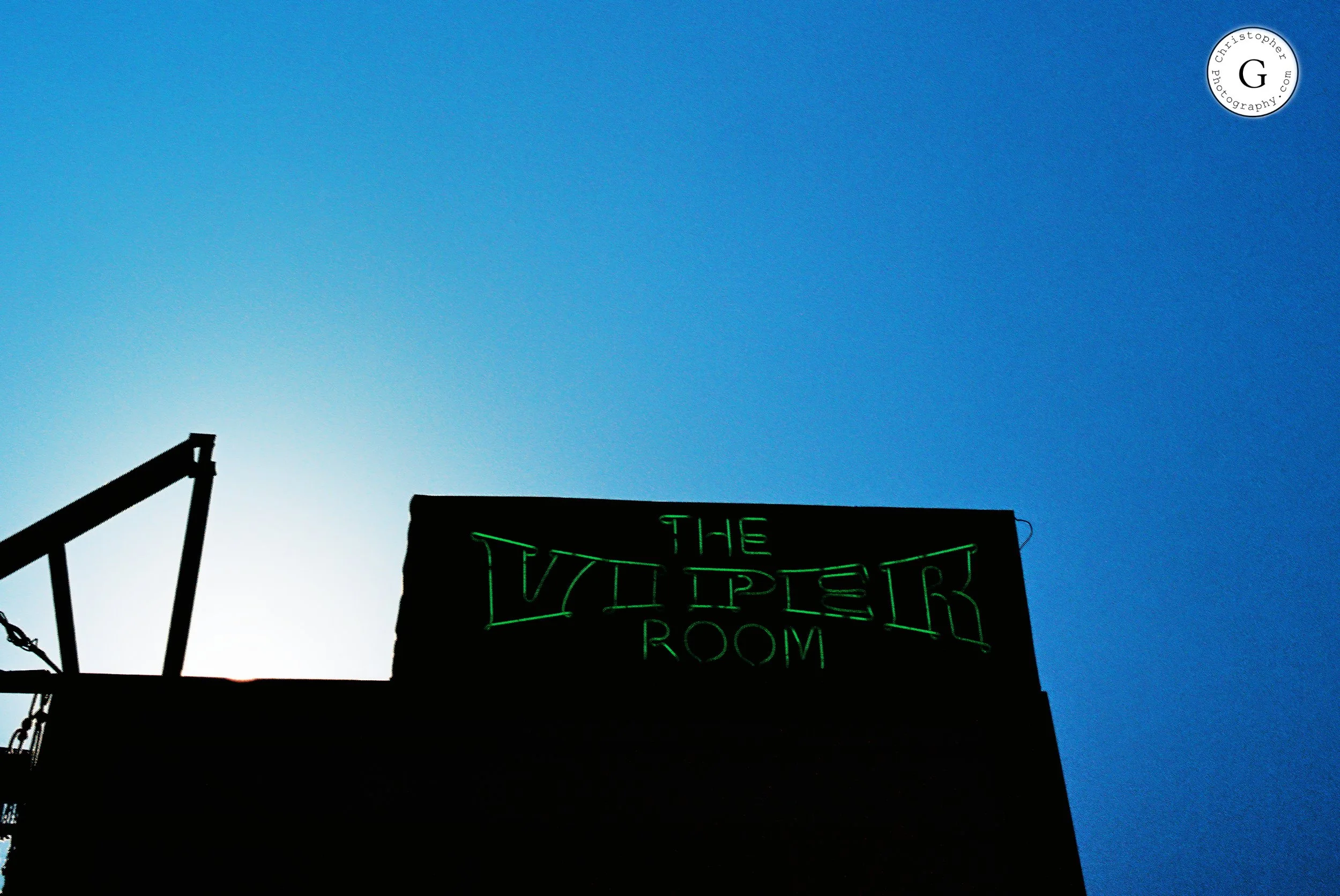 Silhouette of a building with a neon sign that reads 'THE VIPPER ROOM' against a blue sky at dusk shot on 35mm film .