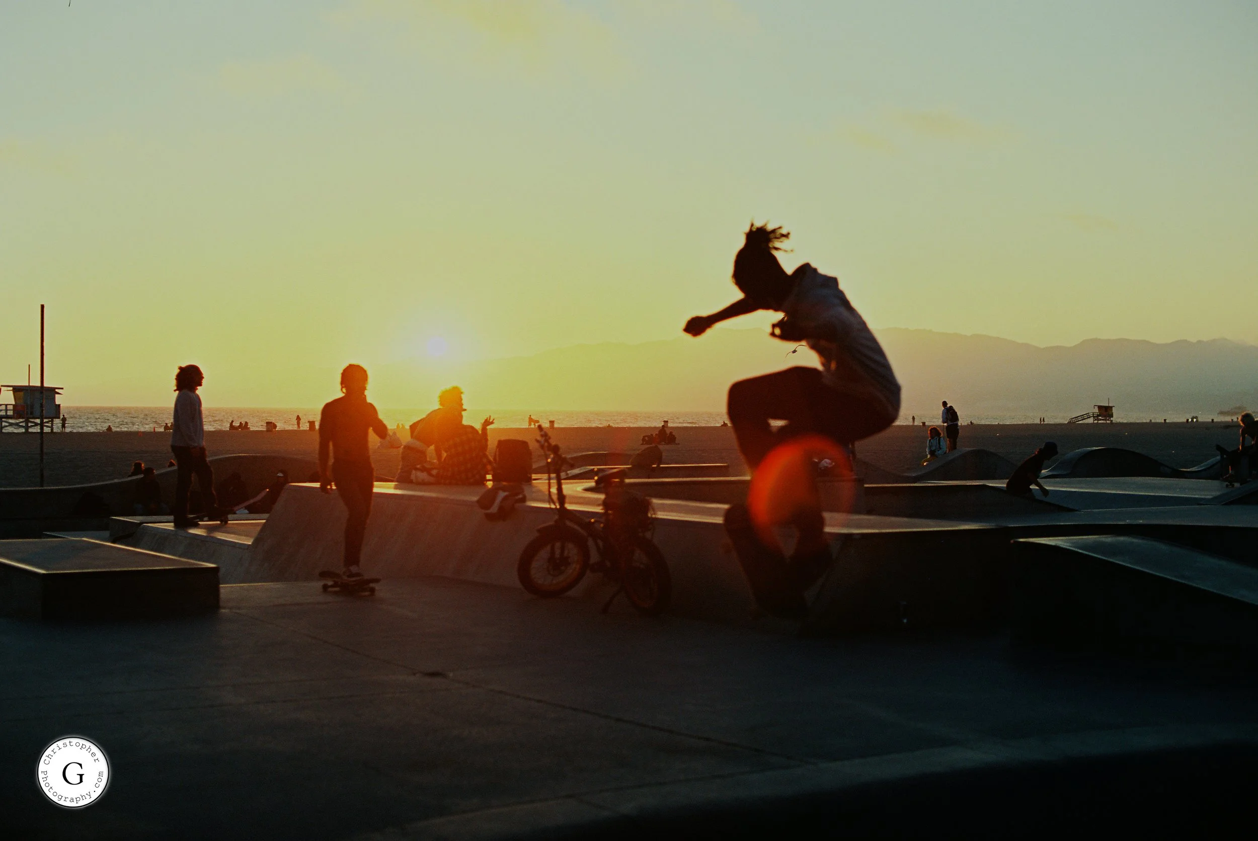 People skateboarding and socializing at a skate park at Venice Beach during sunset shot on 35mm film .
