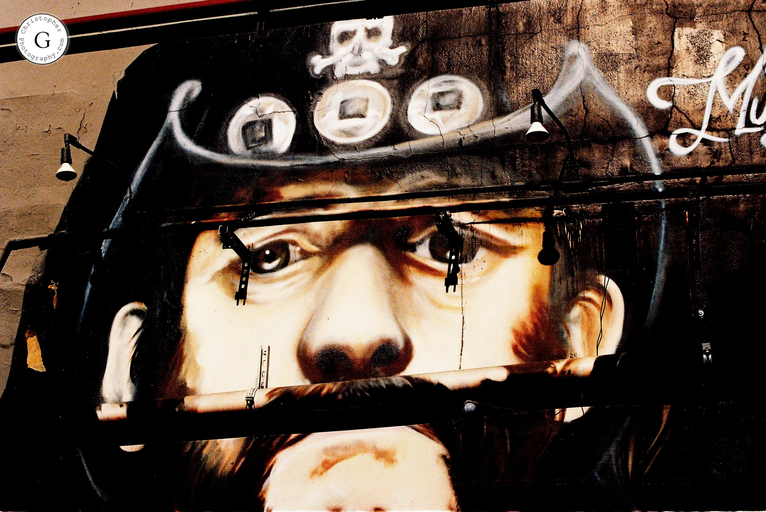 Close-up mural of a person's face with a hat, painted on a wall with graffiti and street art elements, featuring striking eyes and realistic features shot on 35mm film .