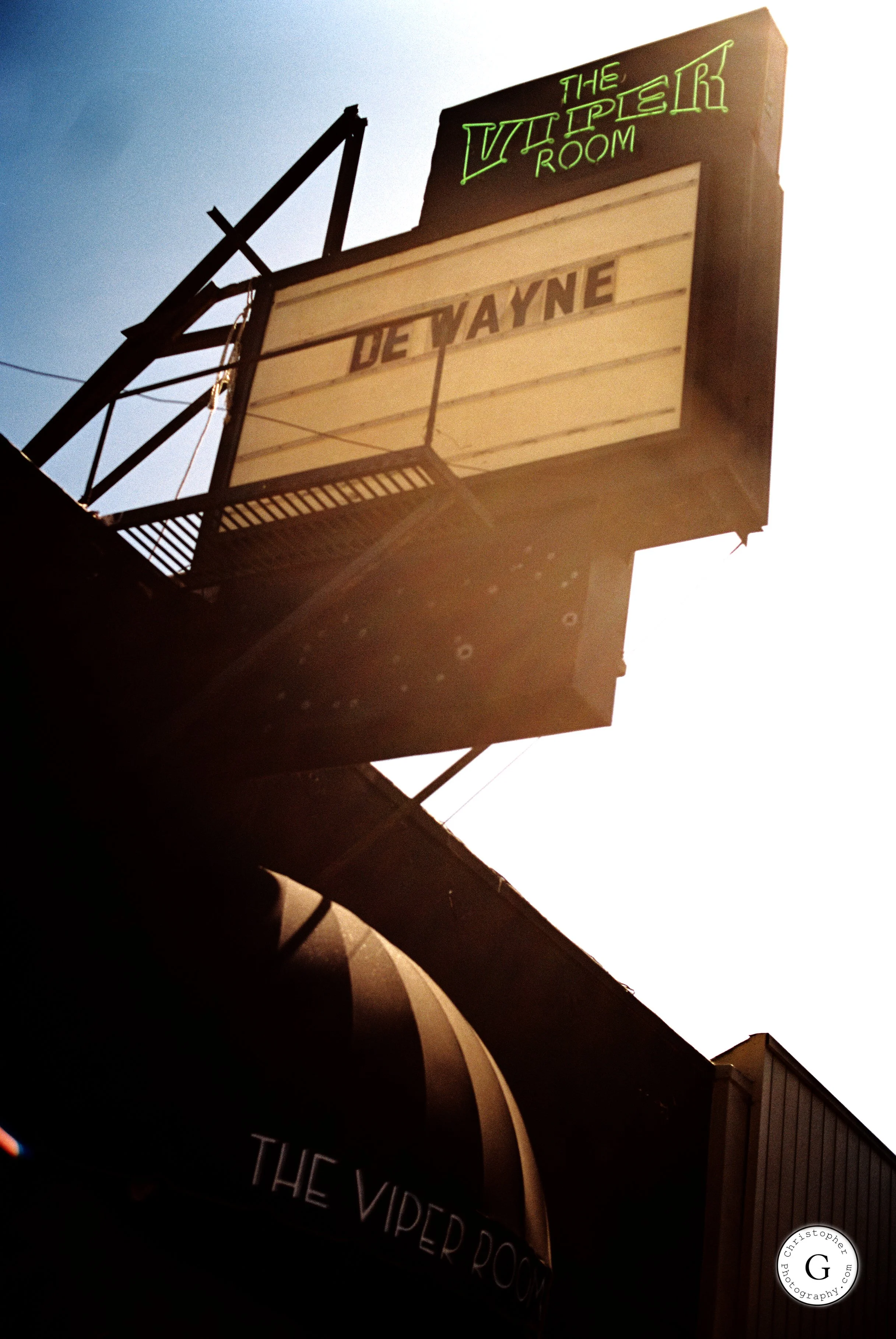 A vintage theater marquee sign reading "The Vampire Room" and "DeWayne" with bright sunlight behind shot on 35mm film.